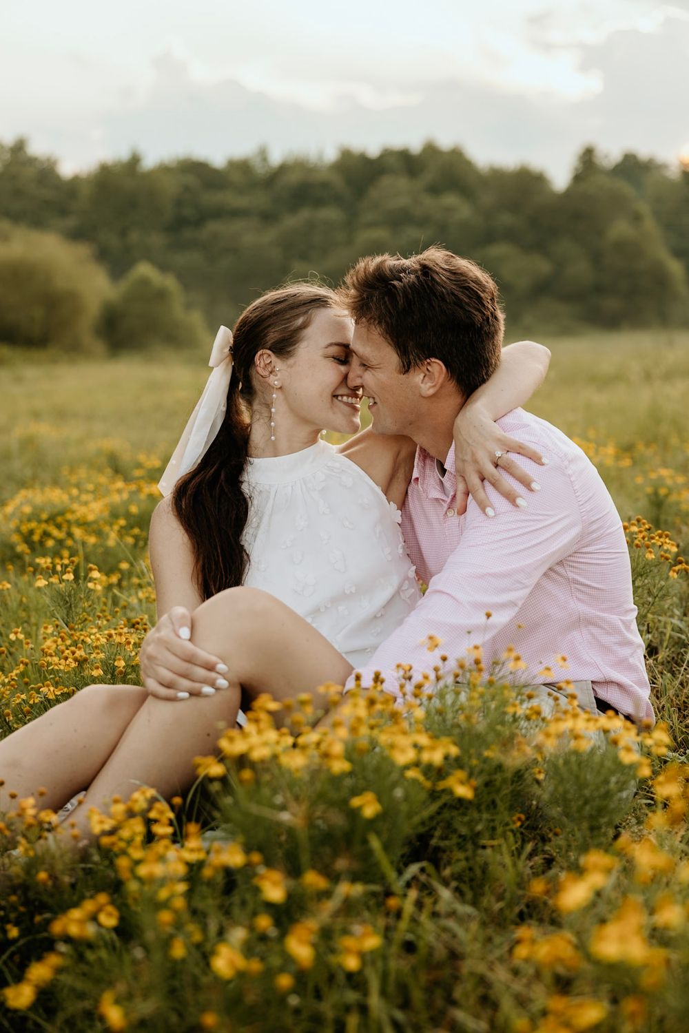 A romantic couple shares an intimate moment while sitting in a field of yellow wildflowers at sunset.