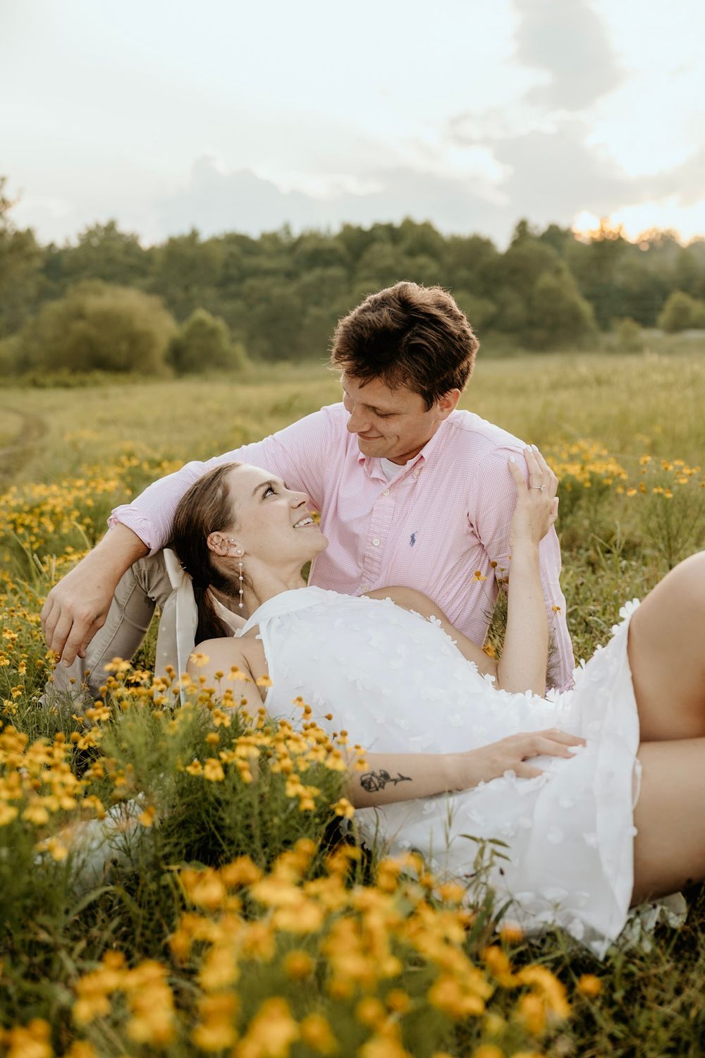 A couple in love lounges together in a meadow filled with golden wildflowers during a summer evening.