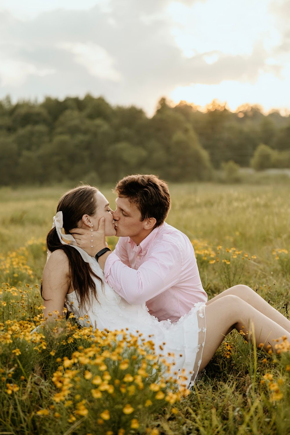 A romantic couple shares a tender moment while sitting in a golden wildflower meadow at sunset.