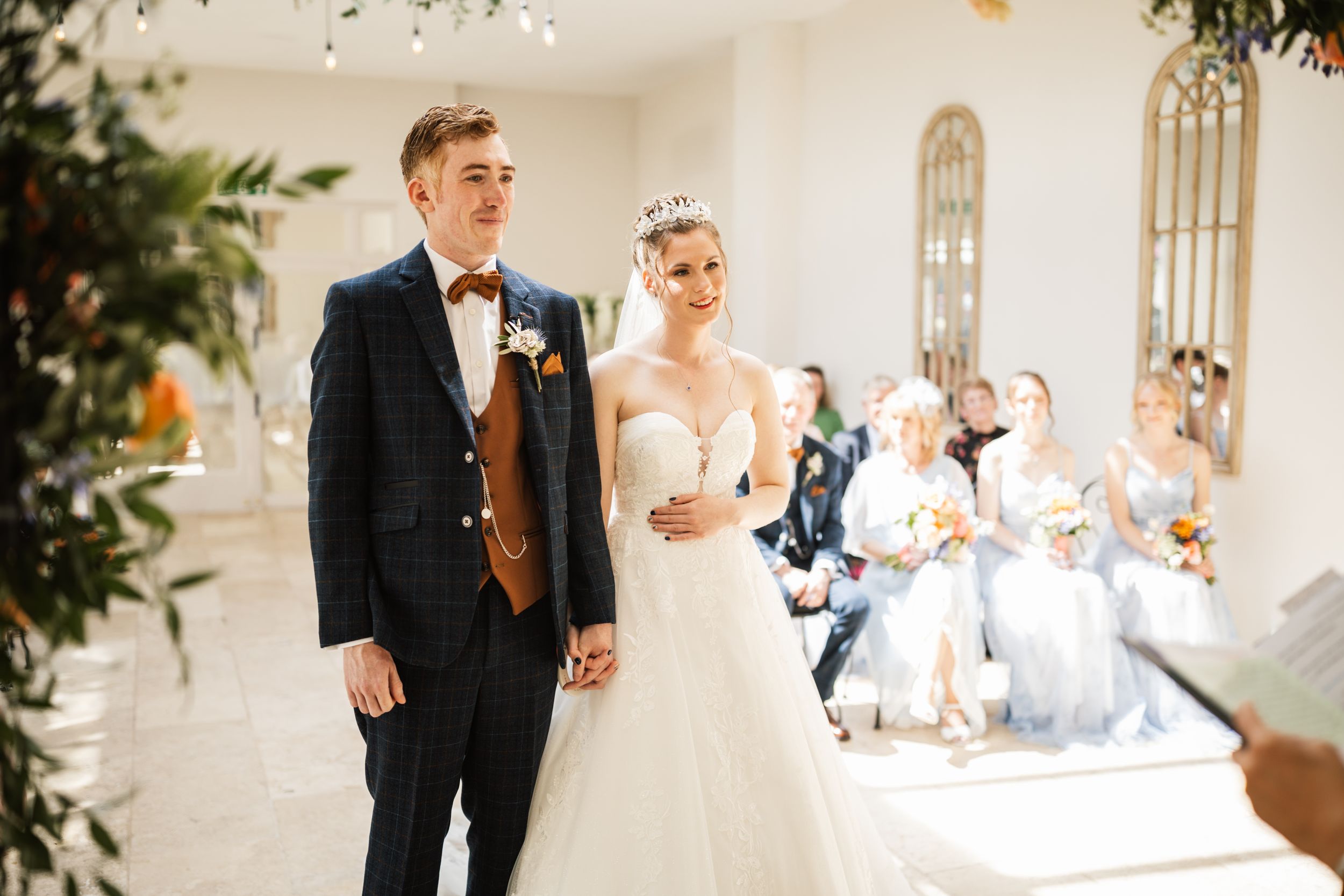 A couple in wedding attire walks down a bright church aisle with guests seated in the background.