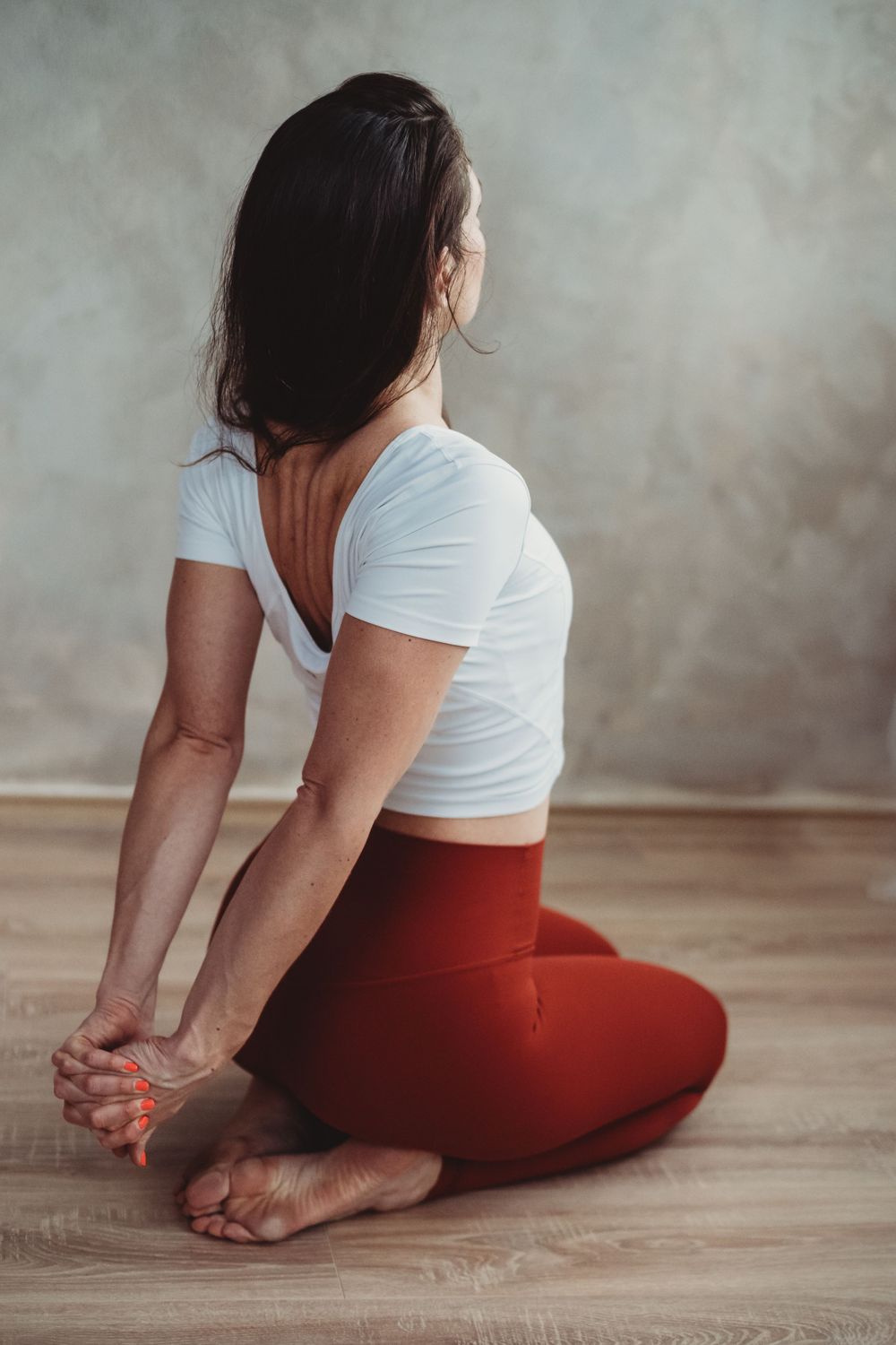 A person practicing yoga on a wooden floor wearing red leggings and a white top in a relaxing pose.
