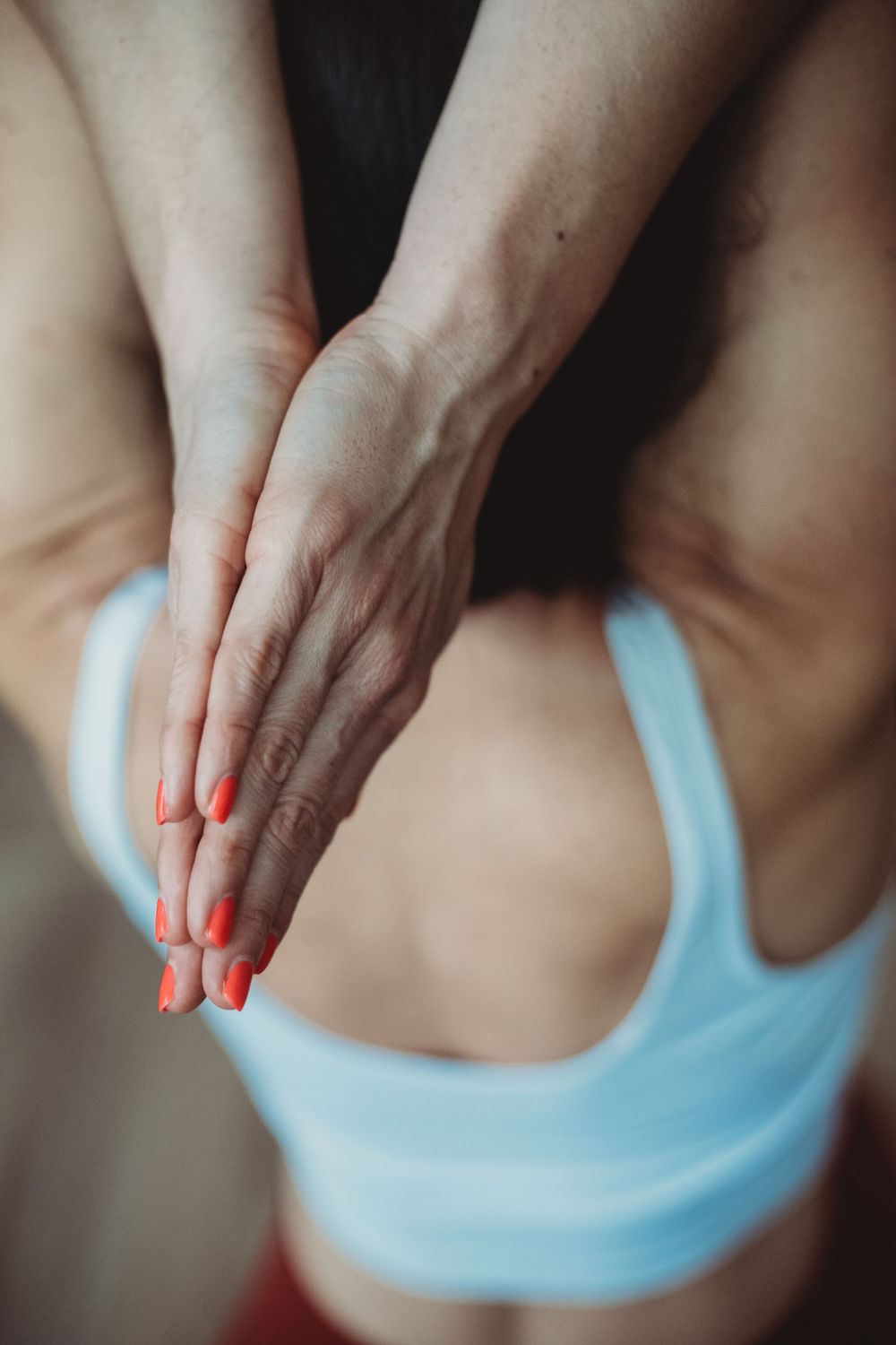 Close-up view of hands clasped over torso wearing light blue sports bra, with orange painted fingernails visible.