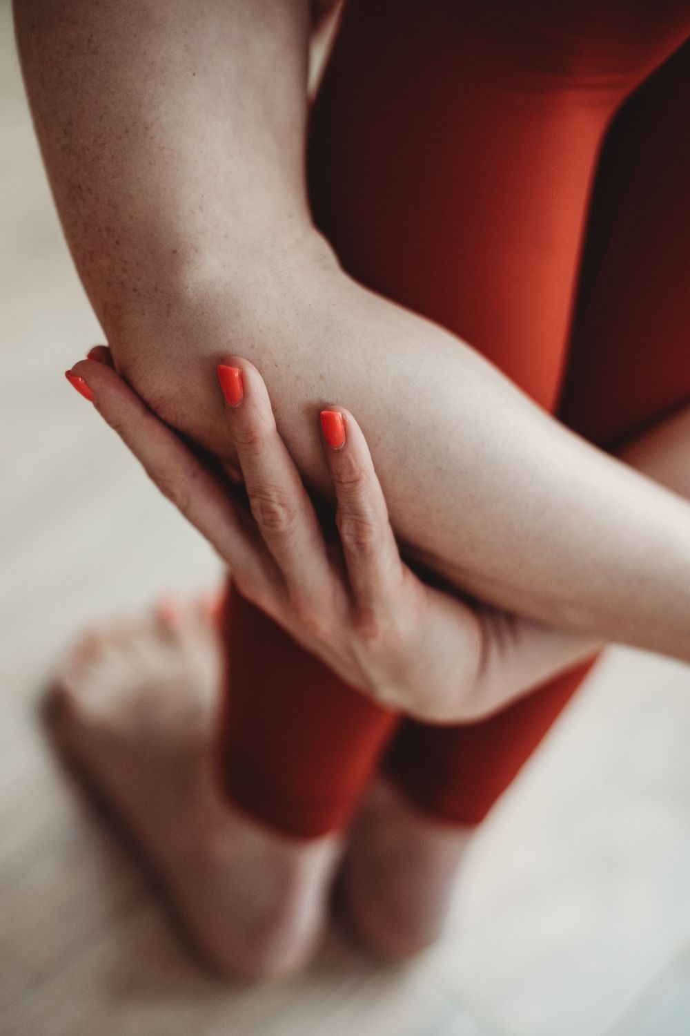 Close-up of hands with bright red nail polish touching bare skin against red clothing and white background.