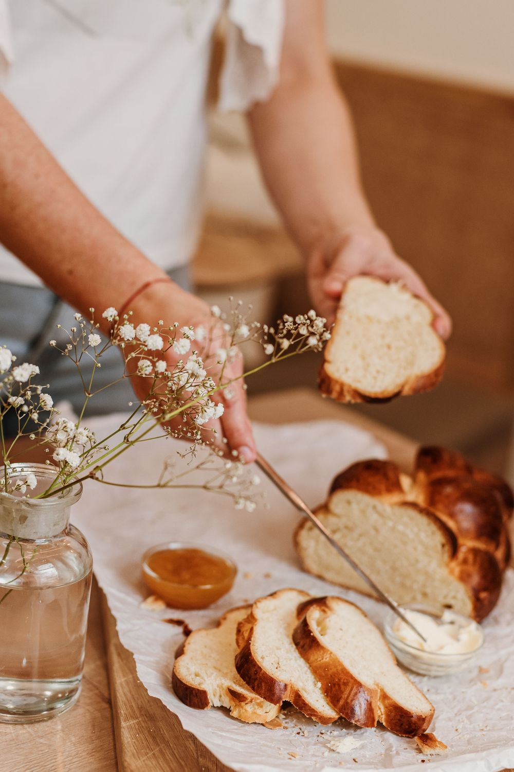 Sliced homemade brioche bread with baby's breath flowers in a vase and honey served on a rustic wooden table.