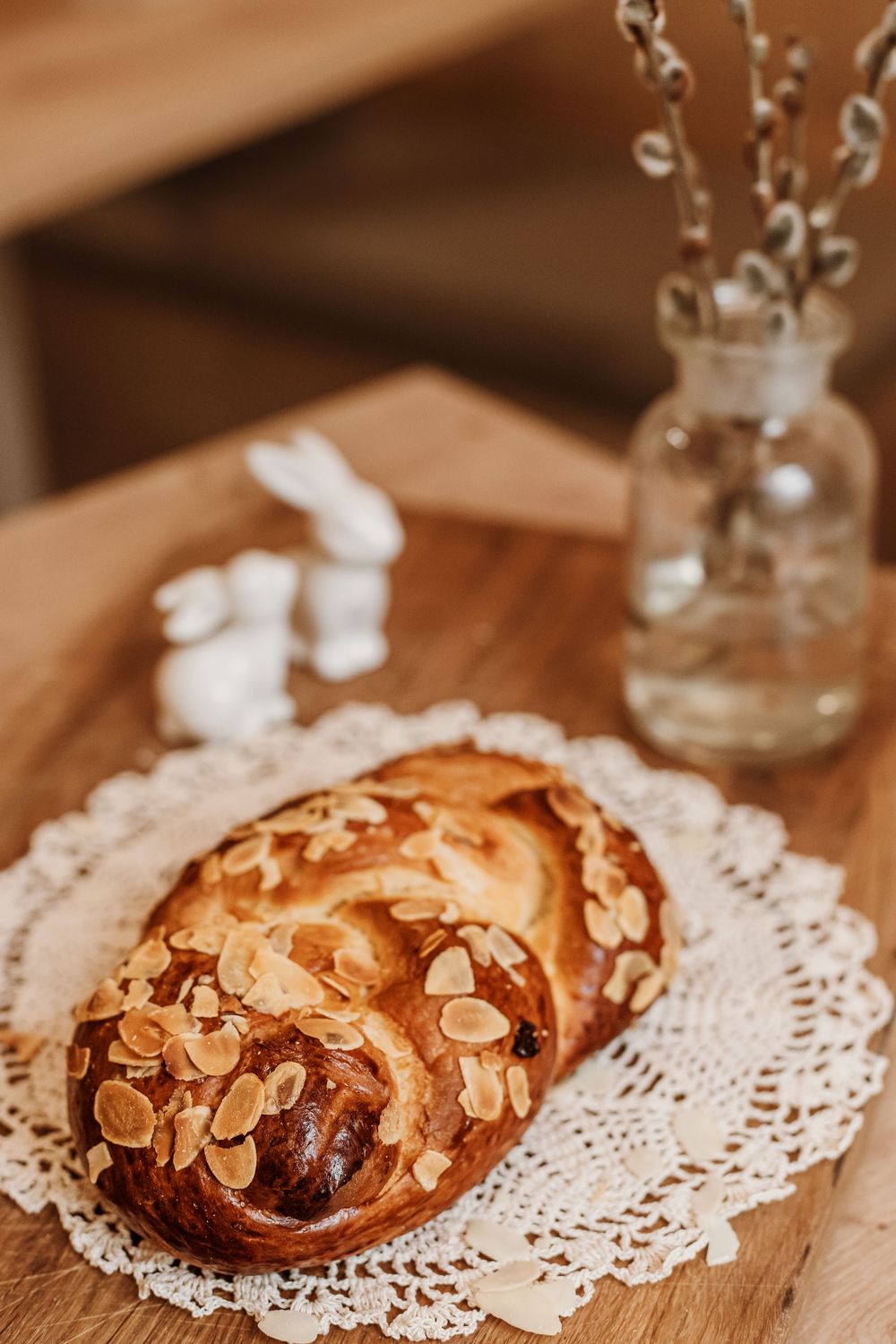 Freshly baked almond crusted pastry on vintage lace doily with decorative glass vase and ceramic bunnies.