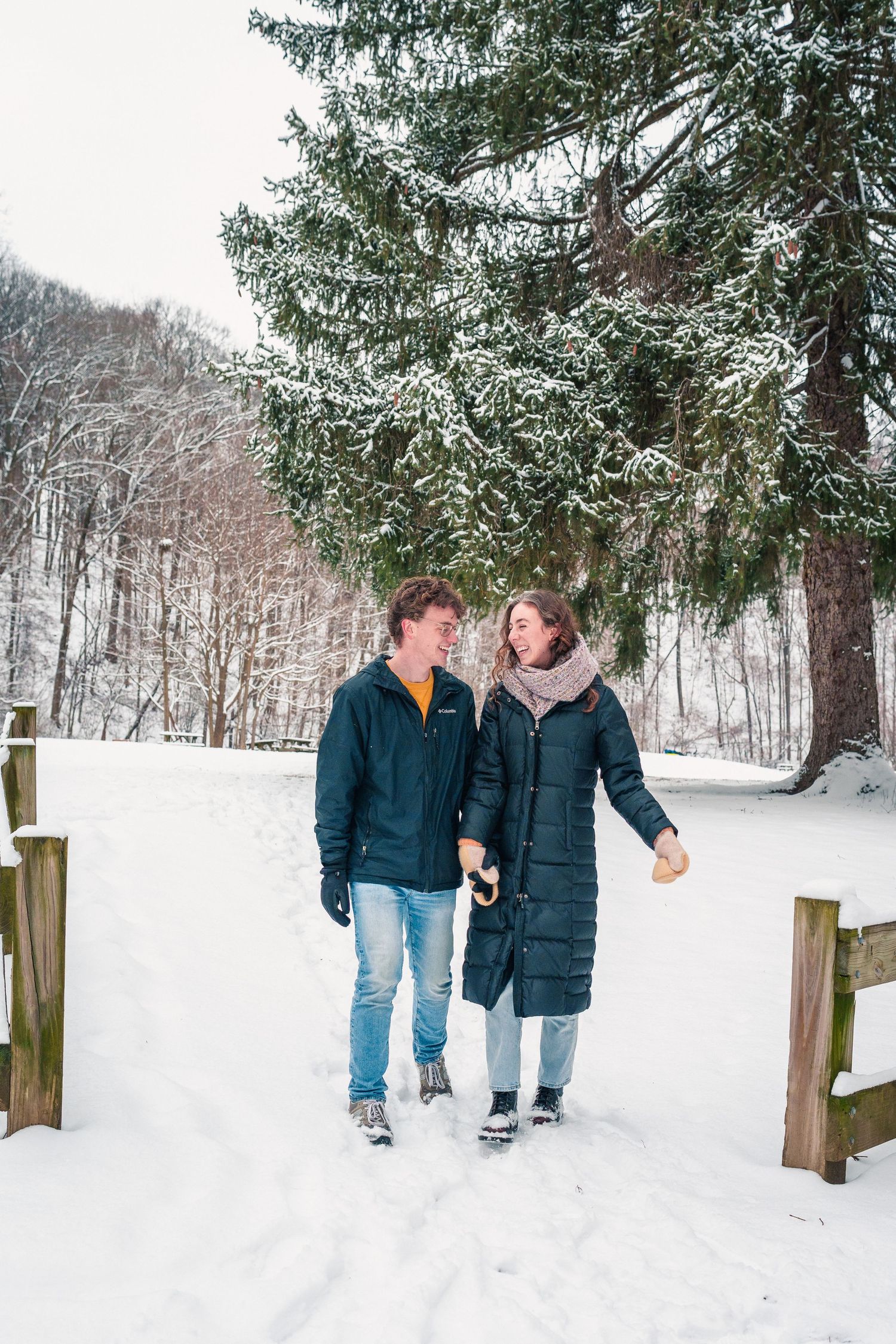 A couple walking together on a snow-covered path through a winter forest landscape.