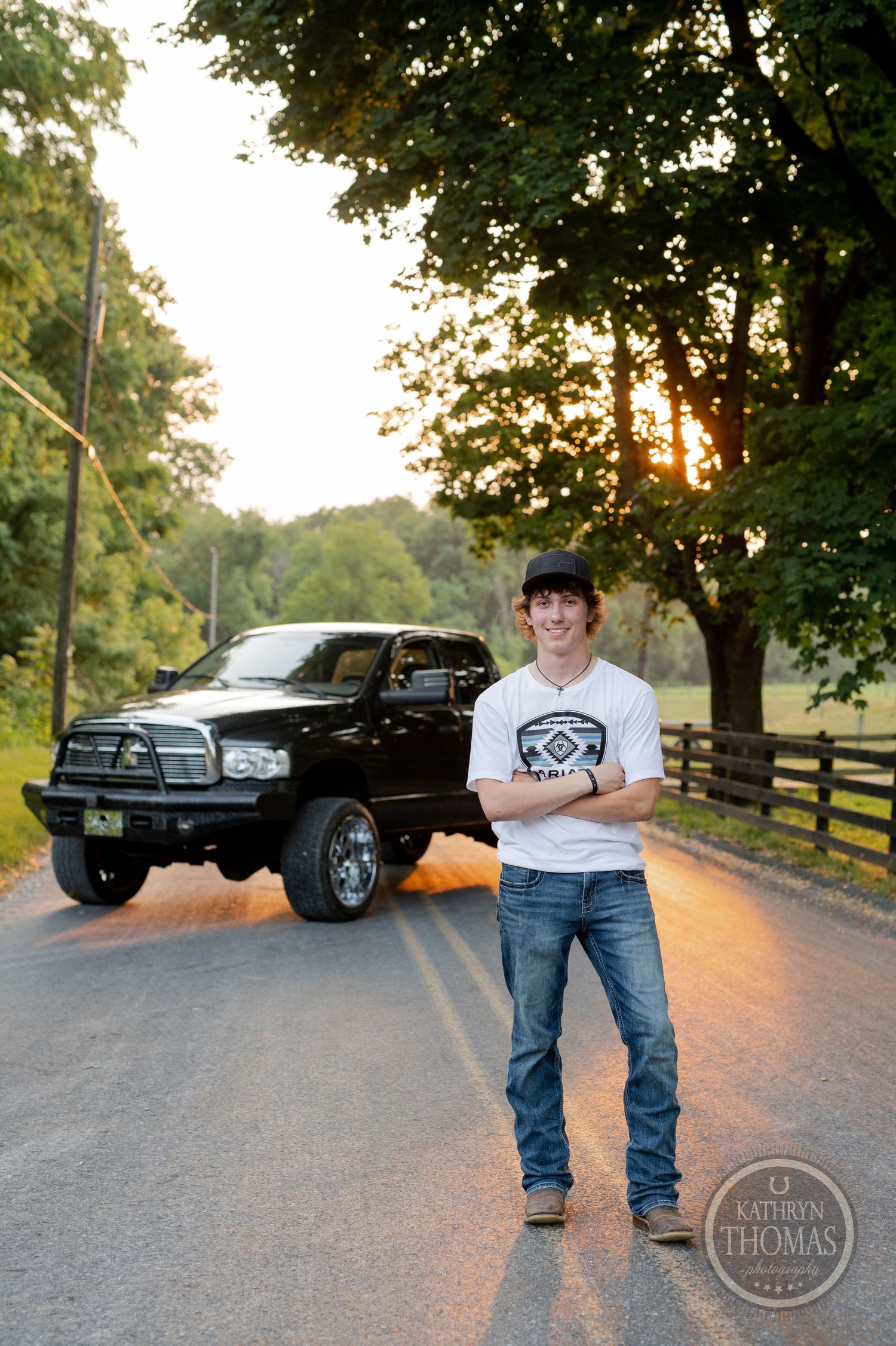 A modified black Dodge Ram truck parked on a country road at sunset.