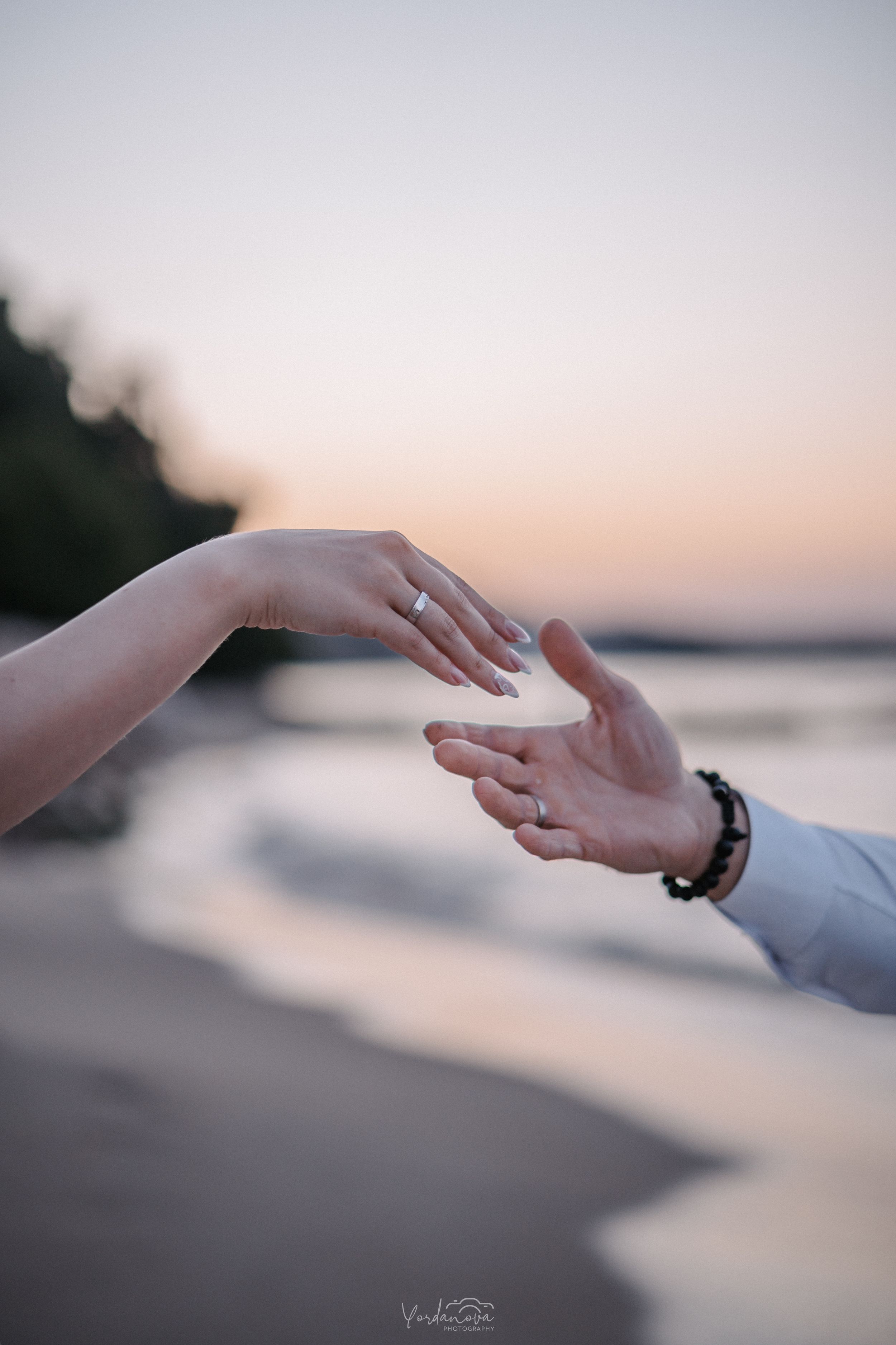 Romantic sunset photo of hands reaching toward each other on beach.