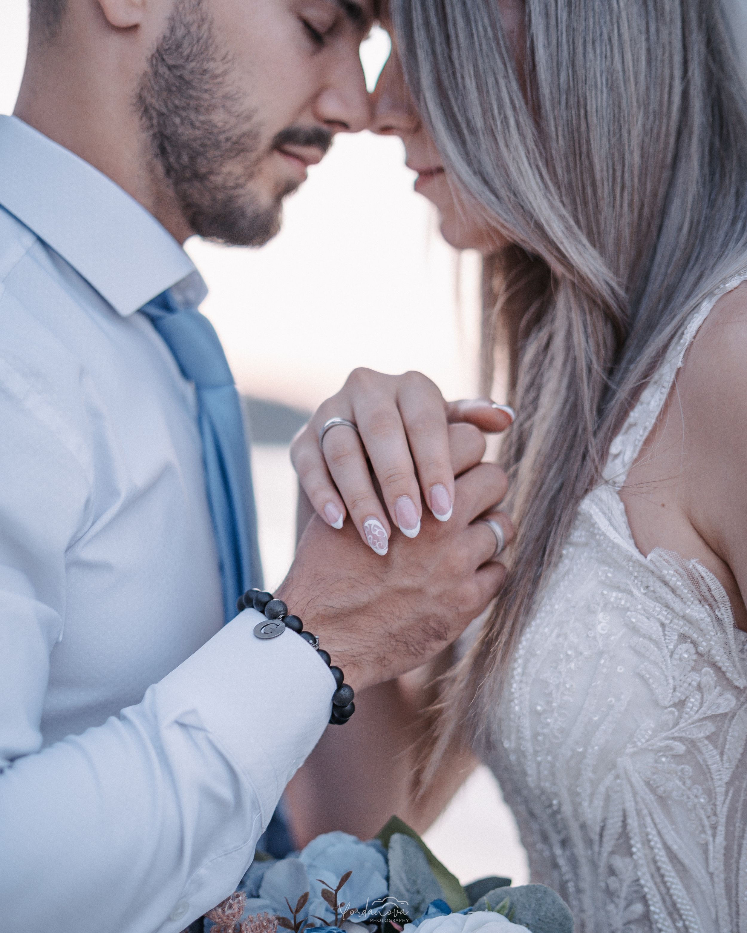 Close up of couple holding hands with engagement ring and bouquet visible.