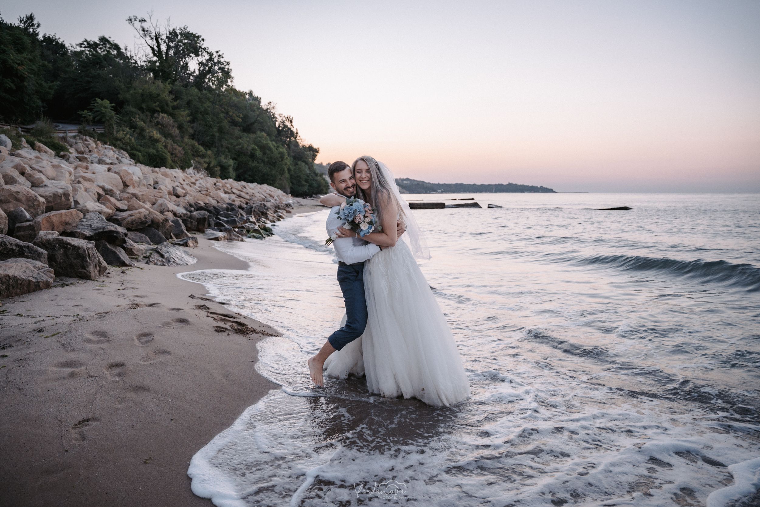 A romantic beach photoshoot at sunset with waves crashing on the shore.