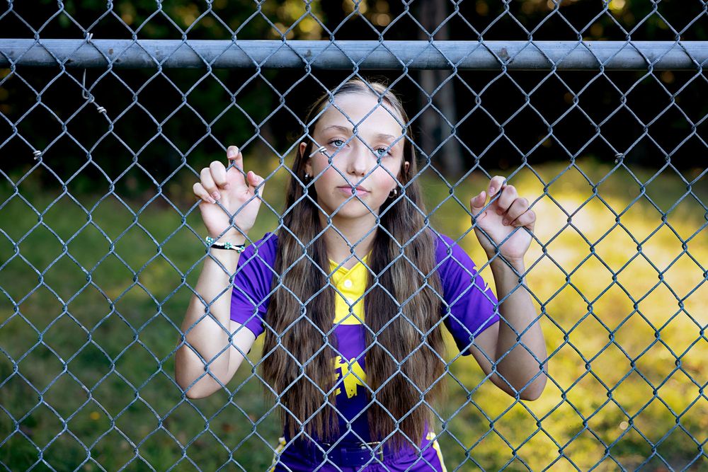 A chain link fence creates a dramatic geometric pattern against a blurred green and yellow background.