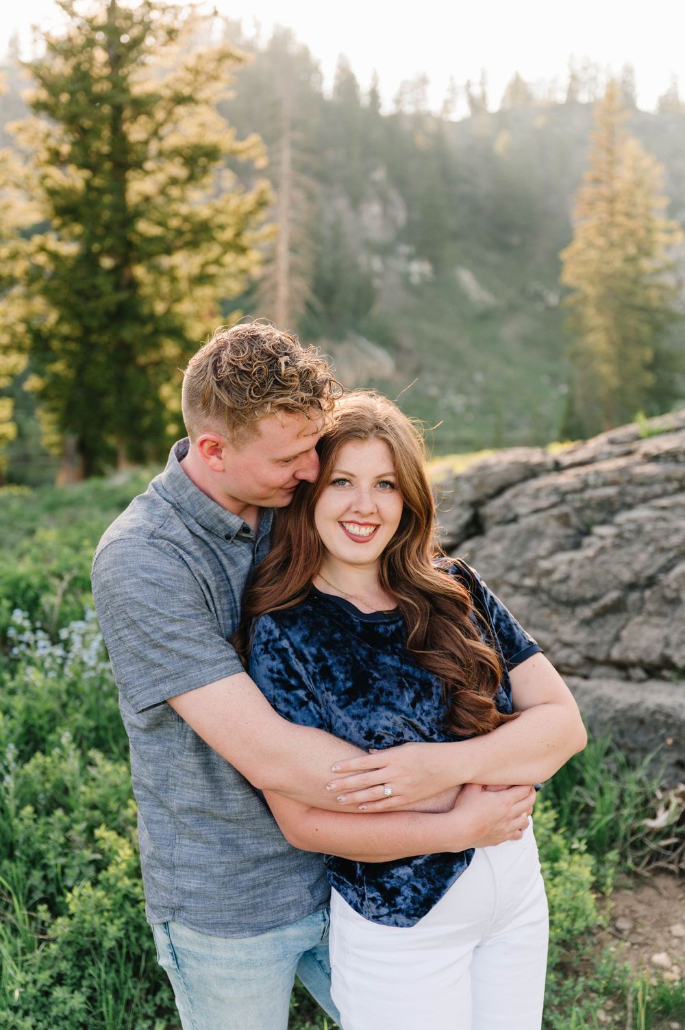 A couple shares an intimate moment against a mountainous forest backdrop.