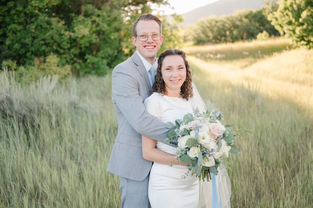 A wedding couple poses in golden mountain meadow at sunset with soft natural lighting.