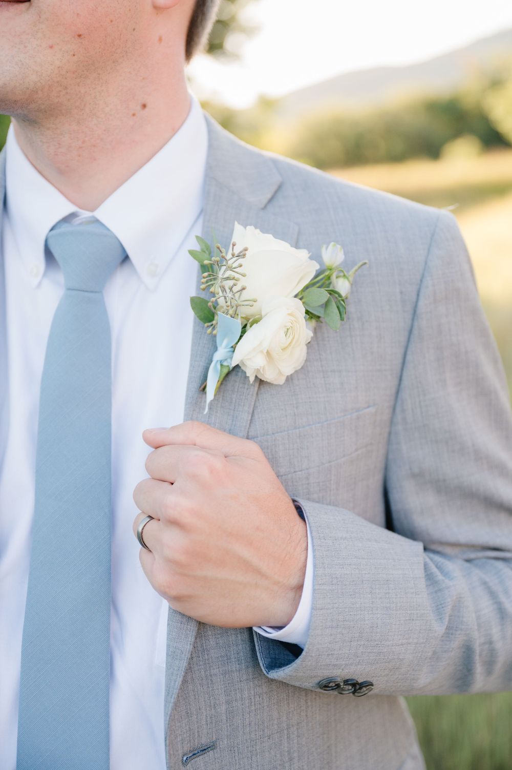 Close-up of groom's white rose boutonniere on light gray suit with blue tie.