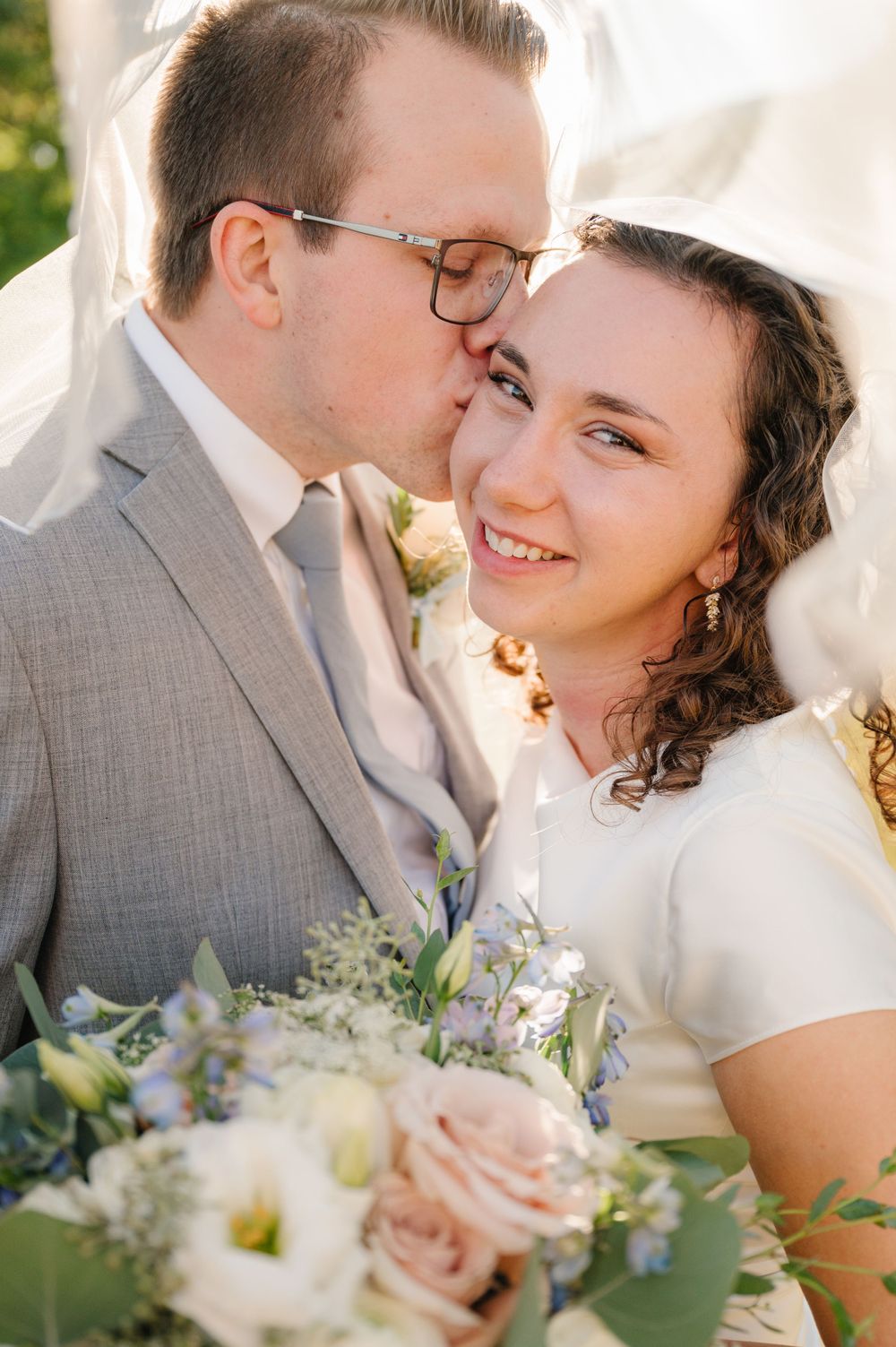 Intimate wedding portrait with soft lighting and pastel floral bouquet in natural setting.