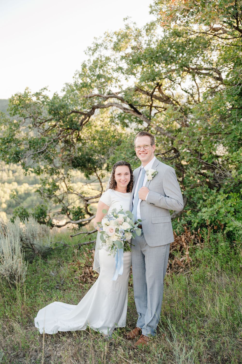 Wedding couple stands together in scenic mountain setting with natural greenery.