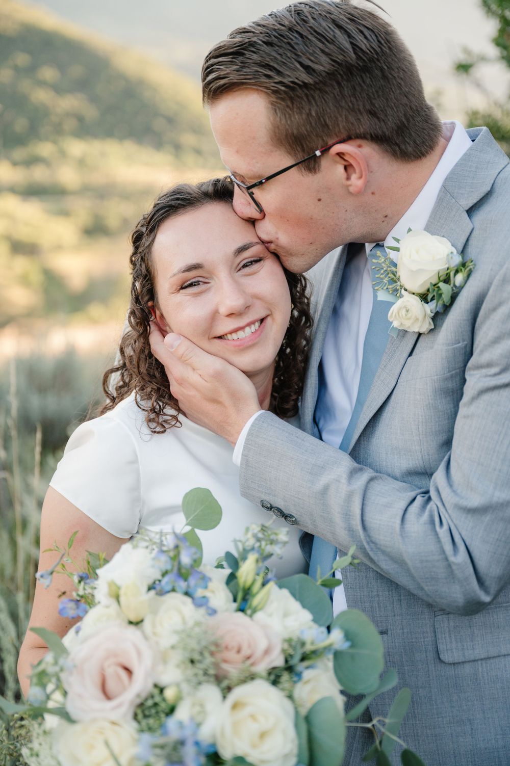 Tender moment captured during outdoor wedding photoshoot with elegant floral bouquet.