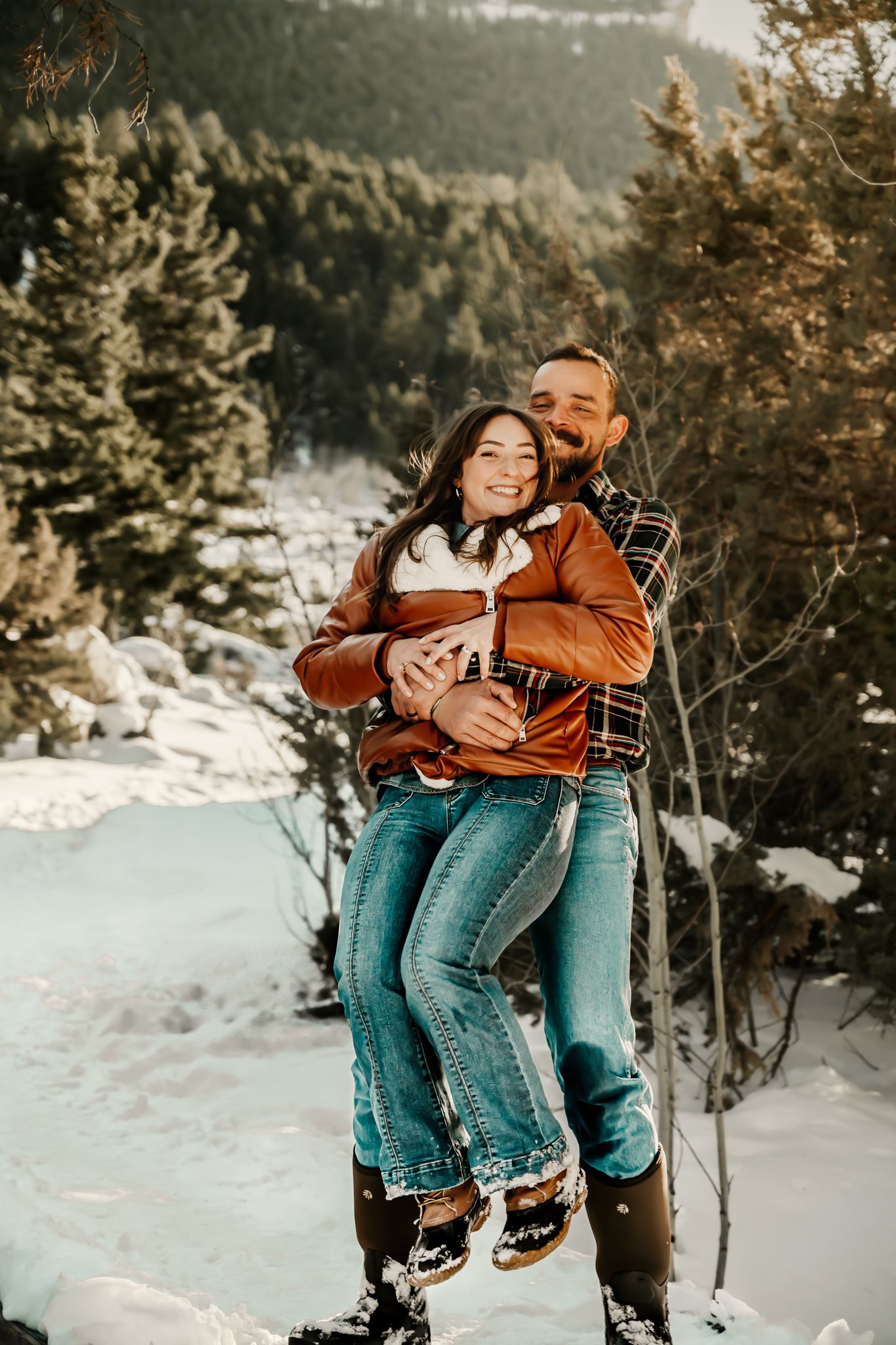 Intimate winter portrait of couple embracing in orange jacket and plaid against snowy landscape.