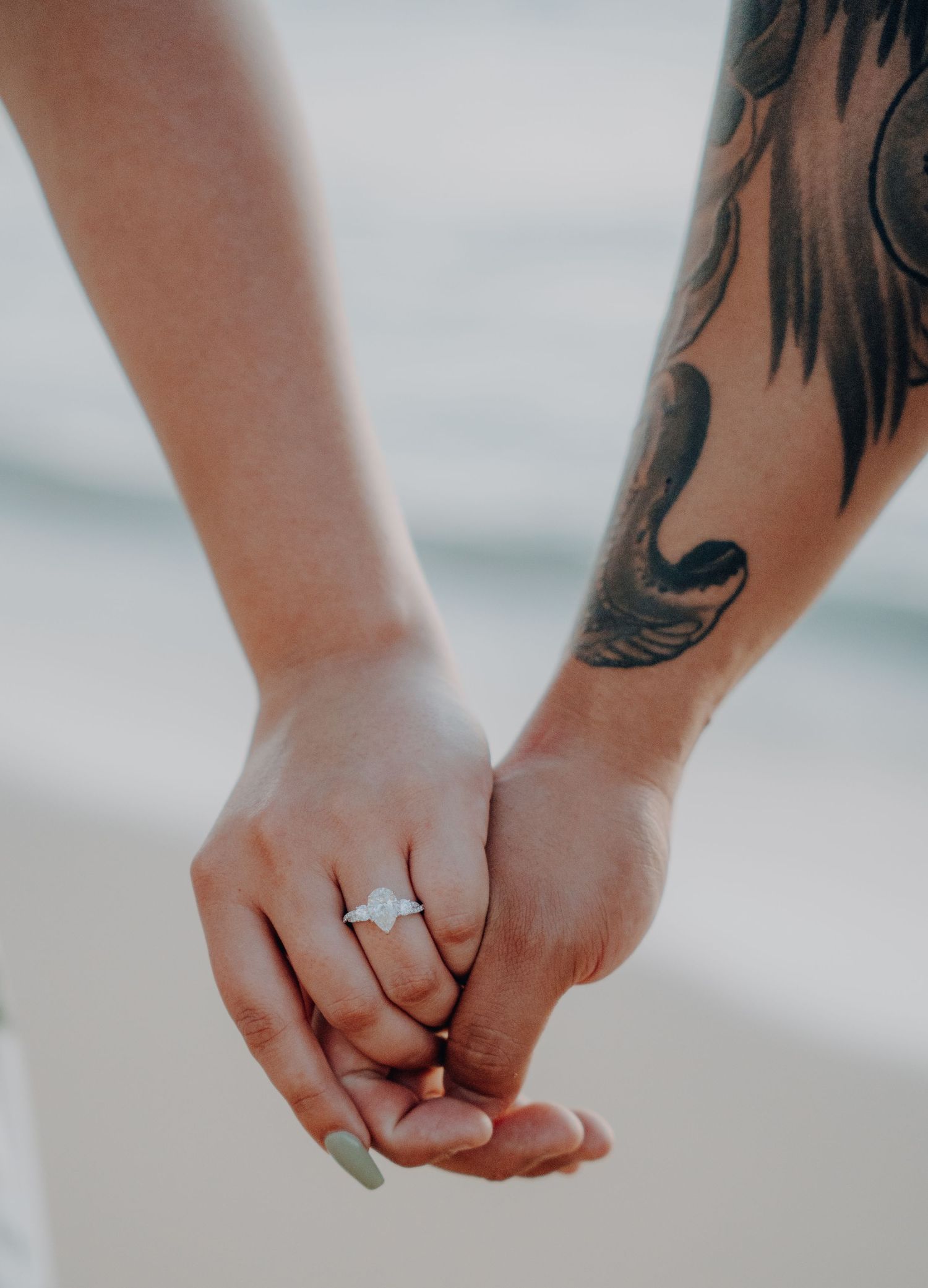 Close-up of two hands holding together, one with a tattoo and an engagement ring.