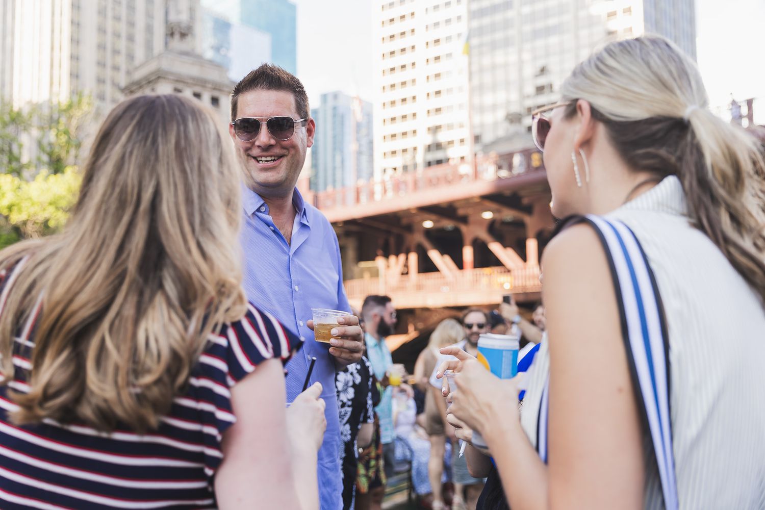 Group socializing outdoors with drinks against Chicago cityscape backdrop.