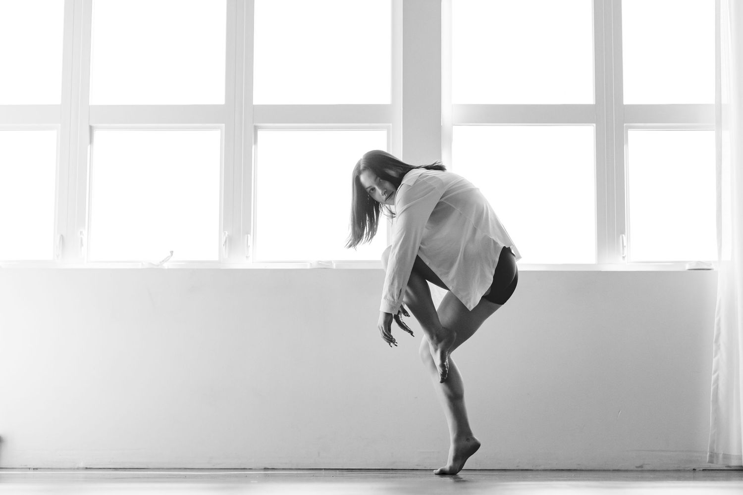 A ballet dancer in white leotard performs an expressive contemporary dance pose in a bright studio setting.