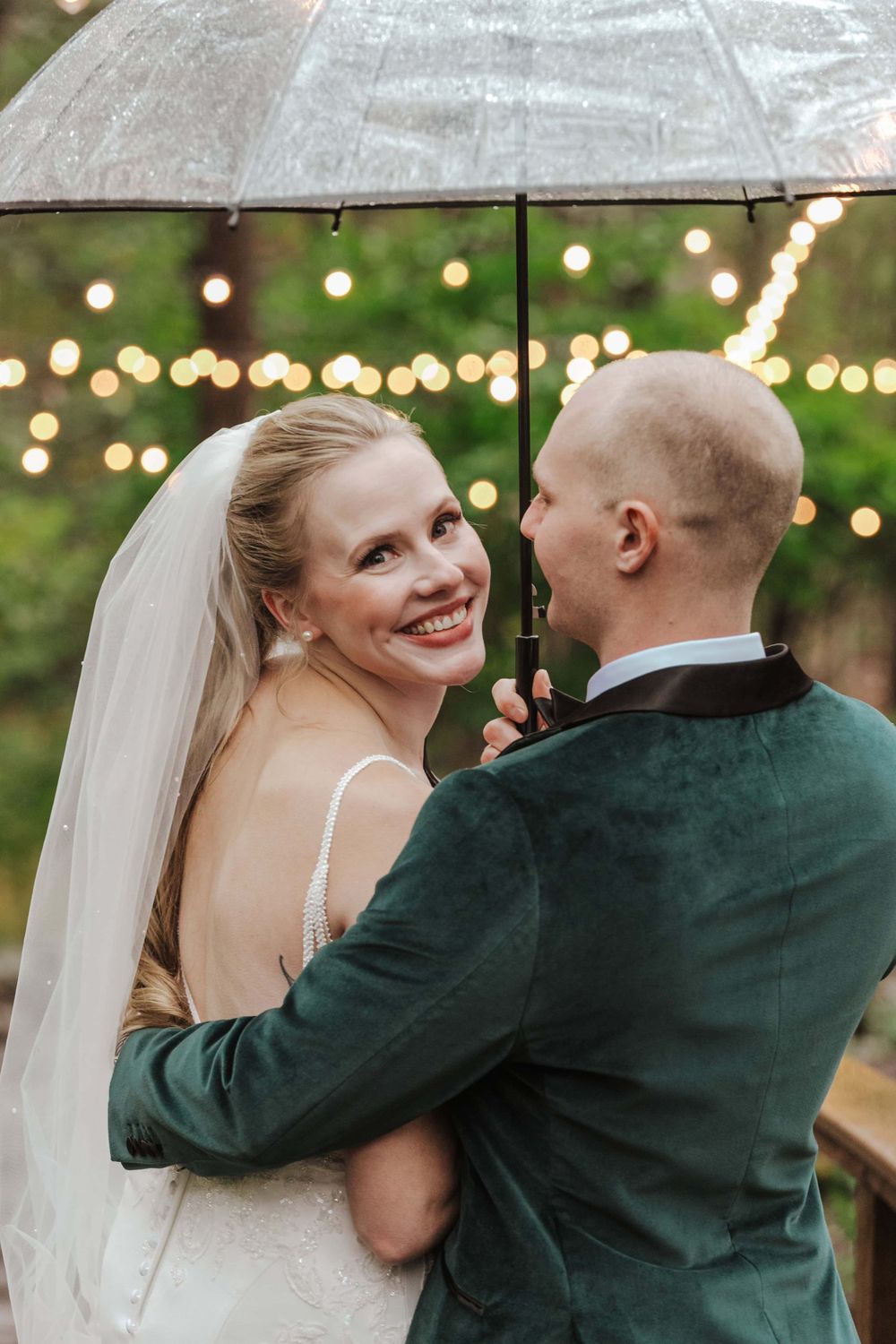Wedding couple shares an intimate moment under an umbrella with twinkle lights in the background.