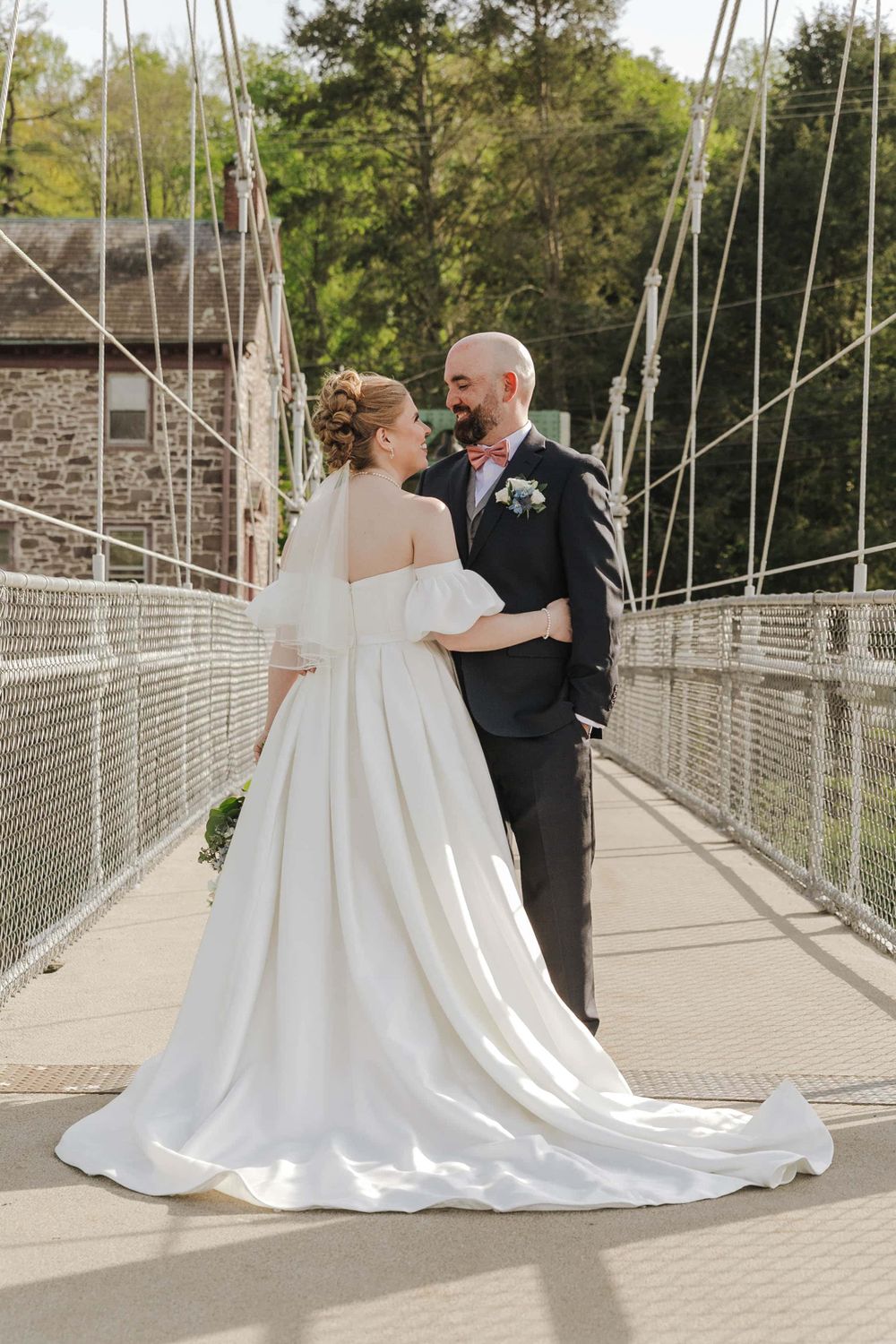 A couple share a romantic moment together on a suspension footbridge in their wedding attire.