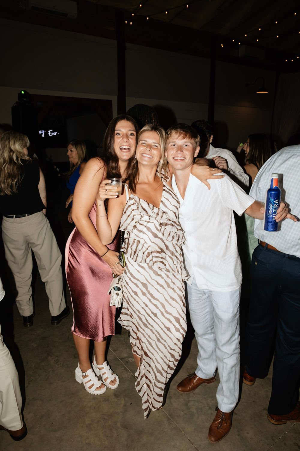 Party guests celebrate at a dimly lit event venue while dancing and socializing.