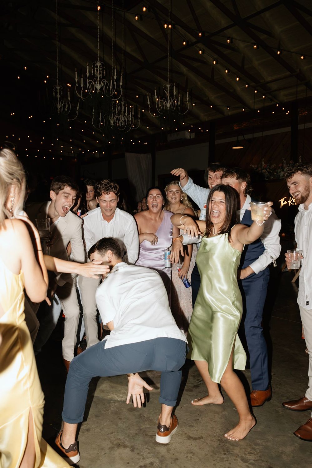 Wedding guests dance and celebrate together on the dance floor under twinkling chandeliers during a reception party.