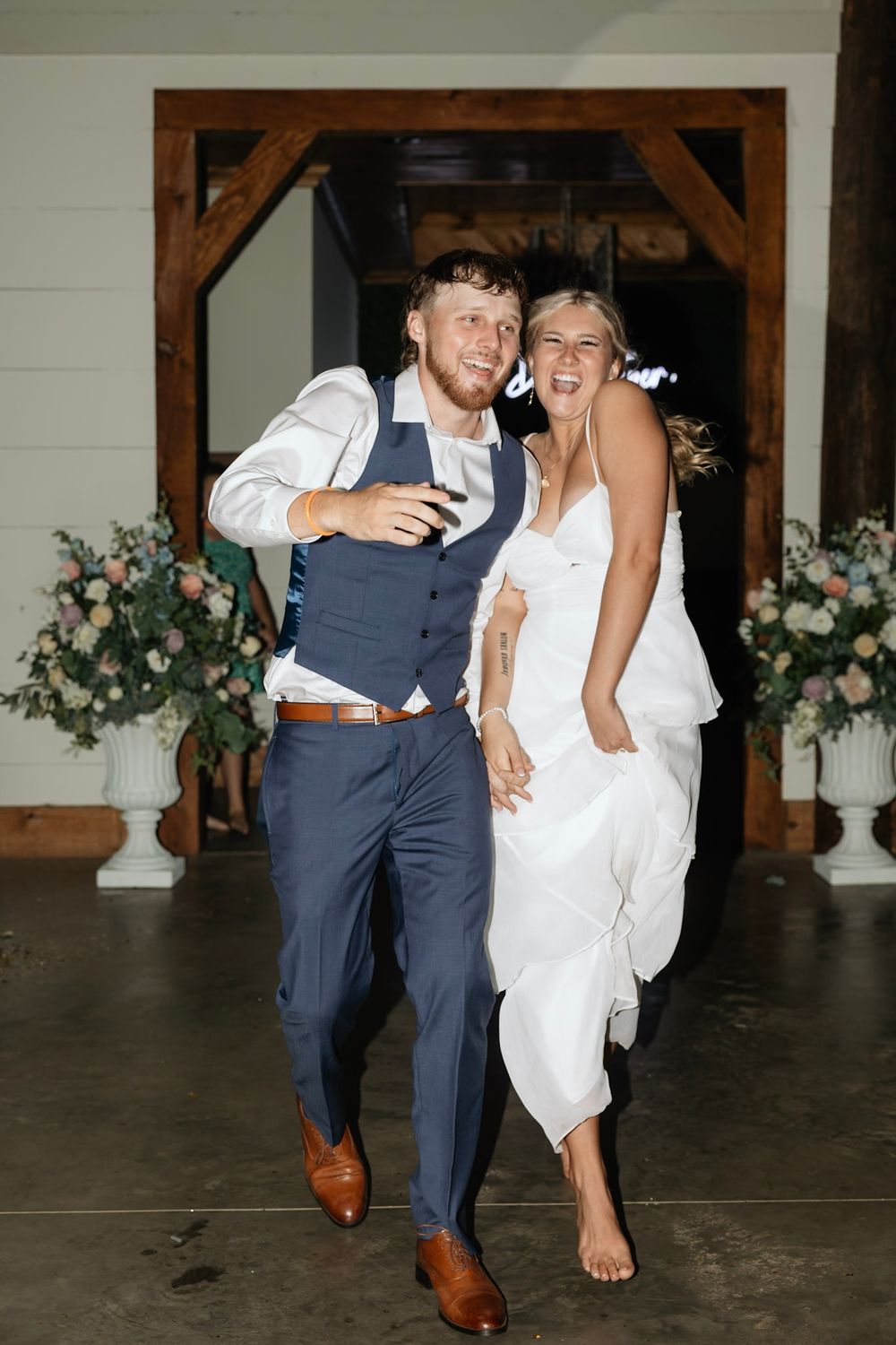 A joyful newlywed couple running and laughing together during their wedding reception.