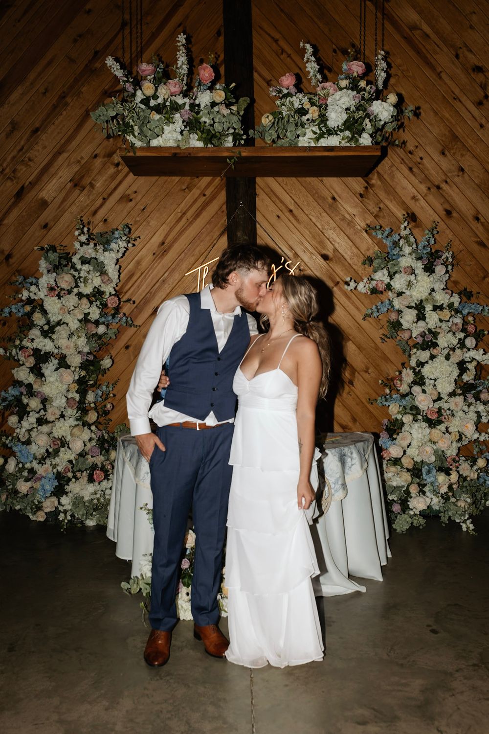 Wedding couple sharing a romantic moment under floral arch with white flowers and green foliage.