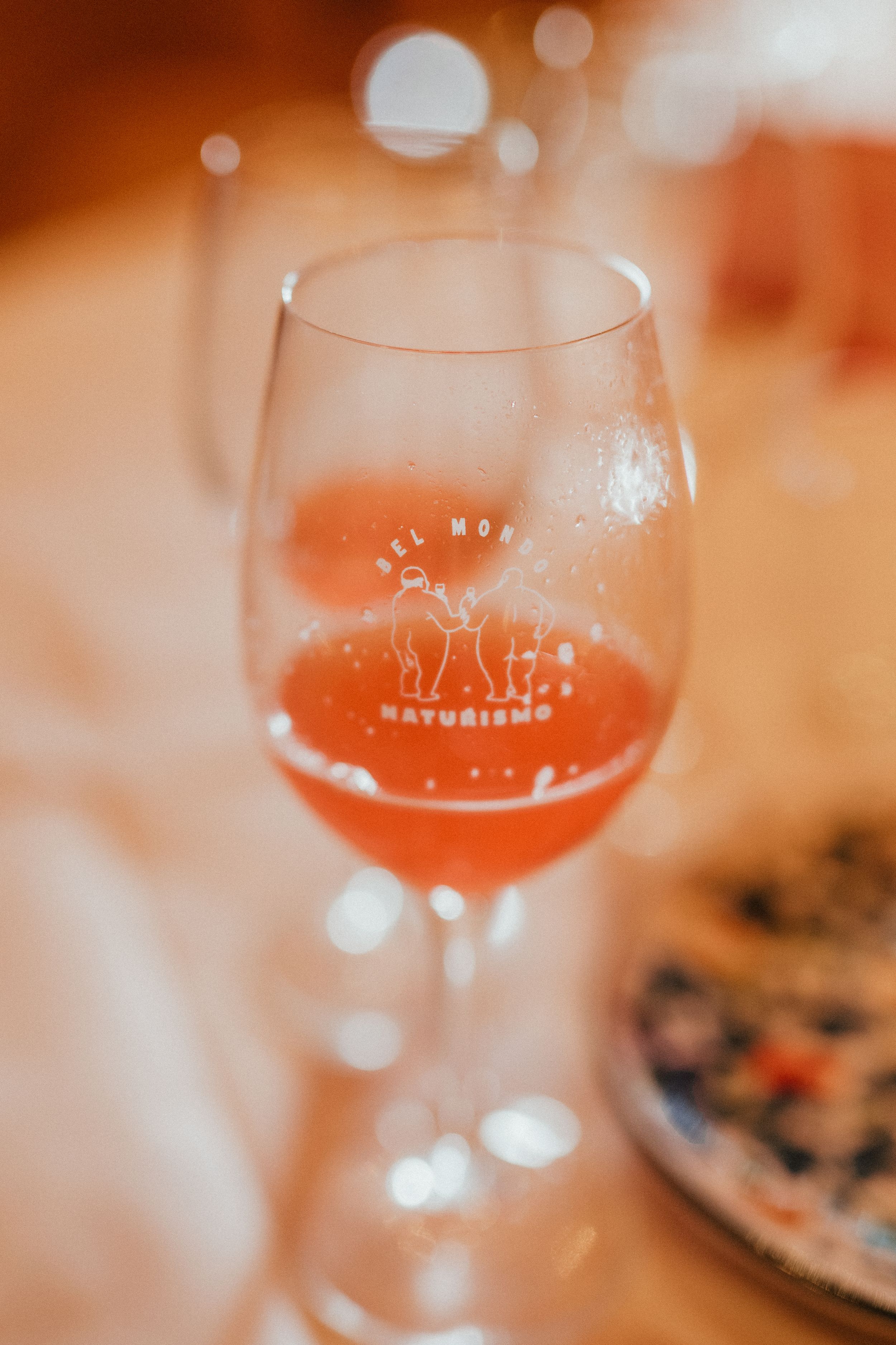 A wine glass containing rose-colored wine with a logo etched on the glass against a warm blurred background.