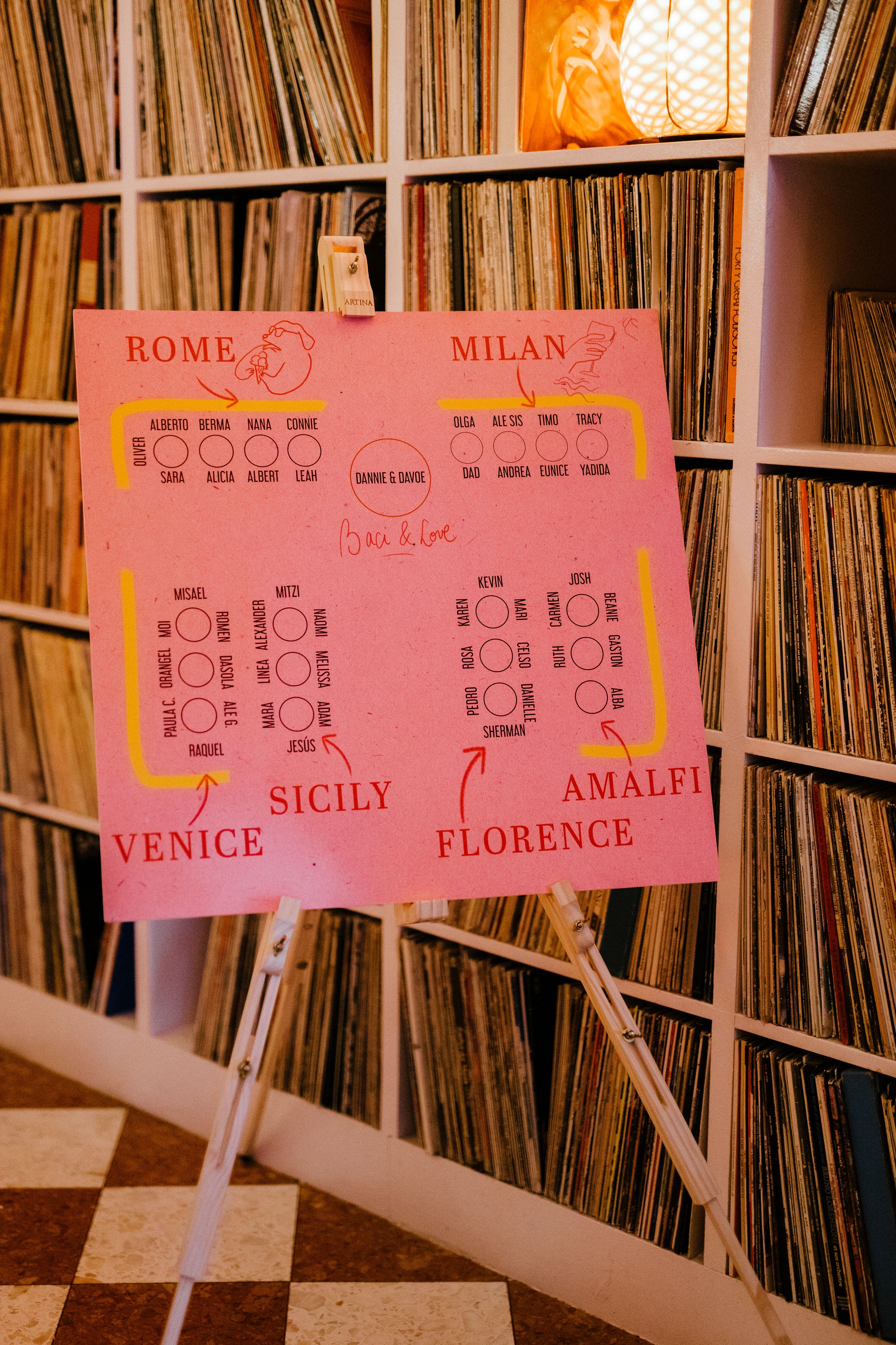 Pink seating chart for Italian cities displayed against vintage vinyl record collection in wooden shelving unit.
