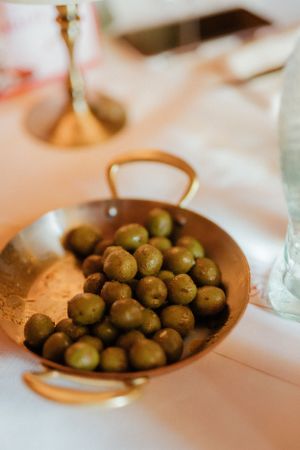 Fresh green olives served in a copper serving dish on a white tablecloth at an elegant dining setting.