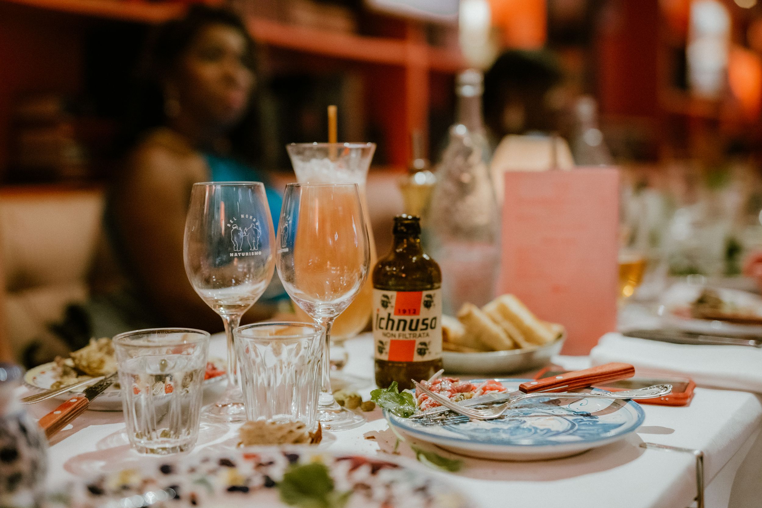 Restaurant table setting with wine glasses, plates, and a Stella Artois beer bottle during a dinner service.
