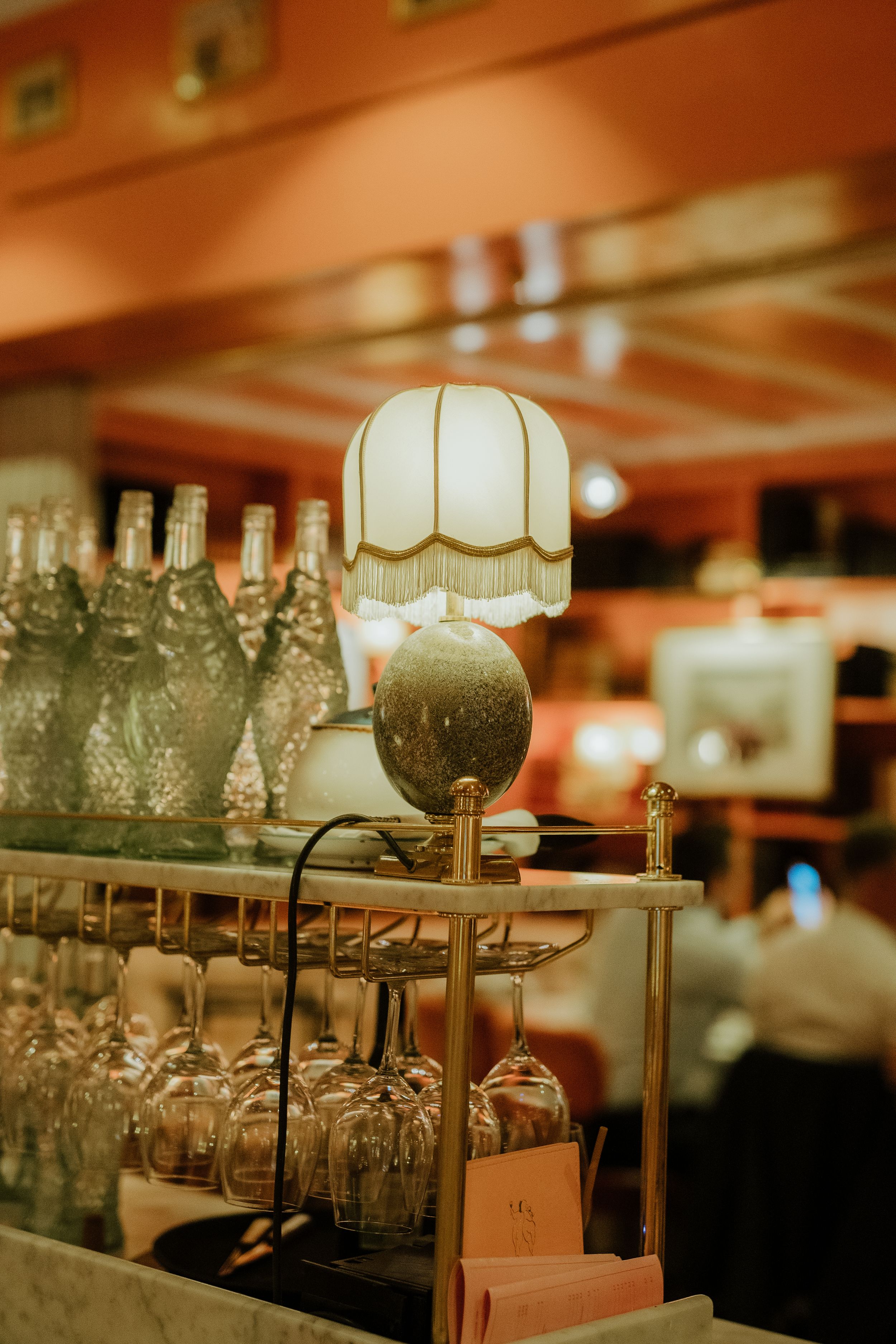 Vintage table lamp and glass bottles in warm lighting create atmospheric bar or restaurant interior decor.