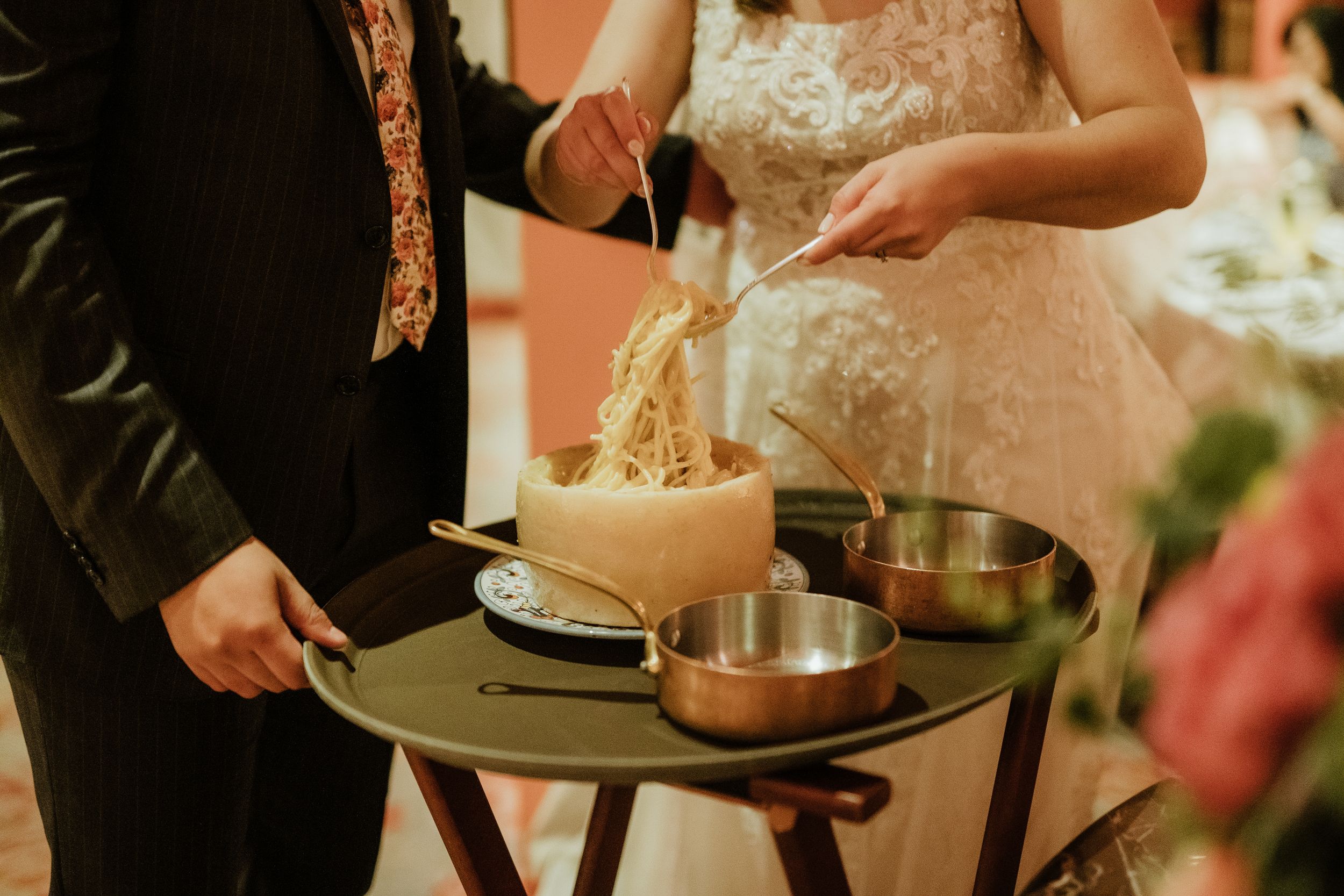 An elegant wedding scene showing hands serving fondue at a reception table with stainless steel pots and warm lighting.