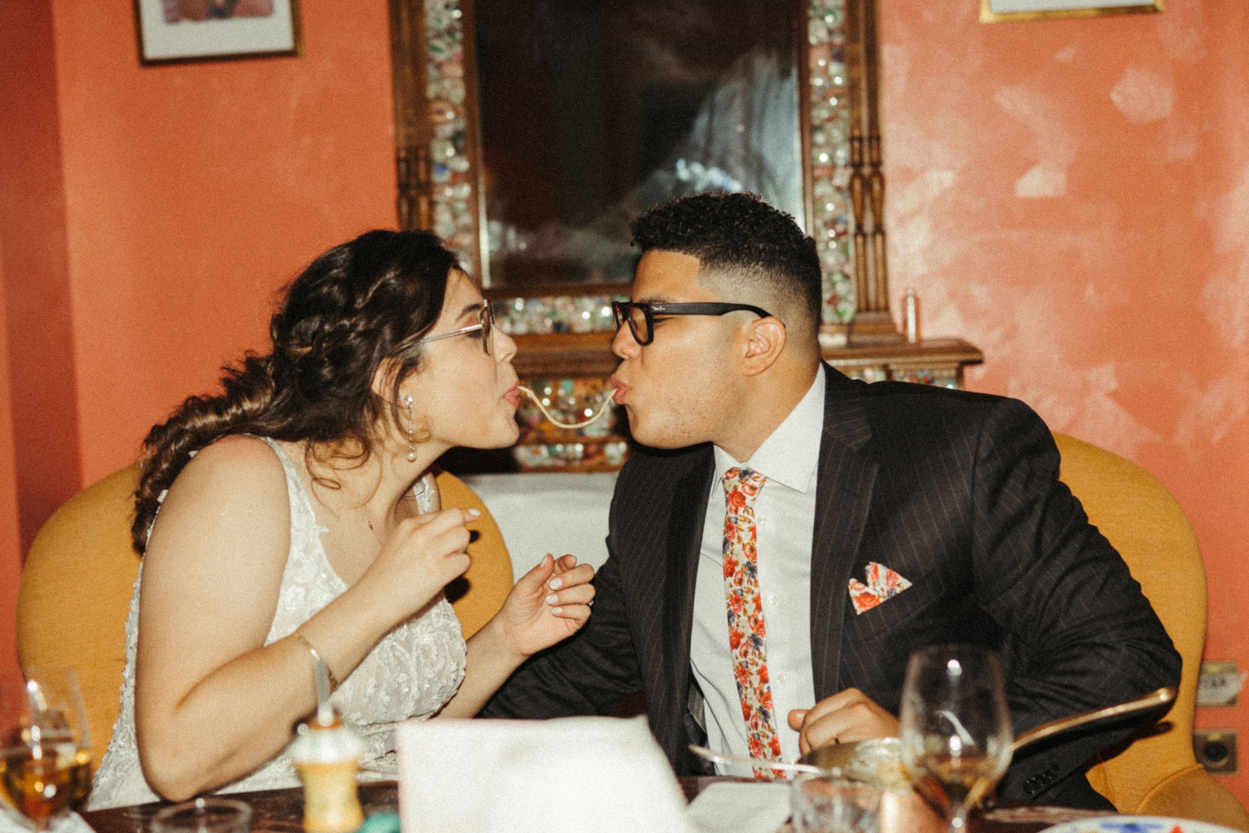 A couple shares a playful moment while dining at a restaurant with orange walls and ornate decor.