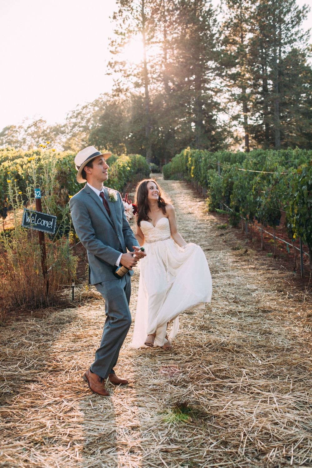Bride and groom walking hand in hand through a vineyard, bathed in warm golden light during their documentary wedding coverage style.