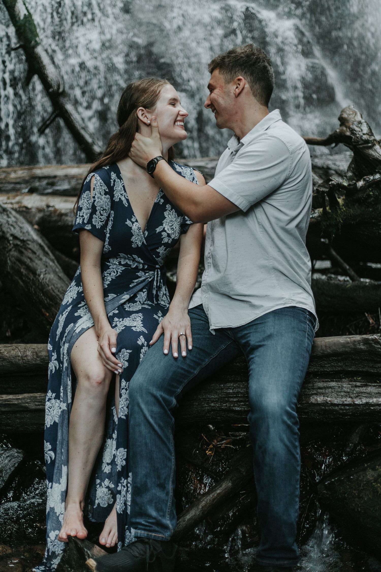 A couple shares an intimate moment while sitting on rocky terrain near a waterfall.