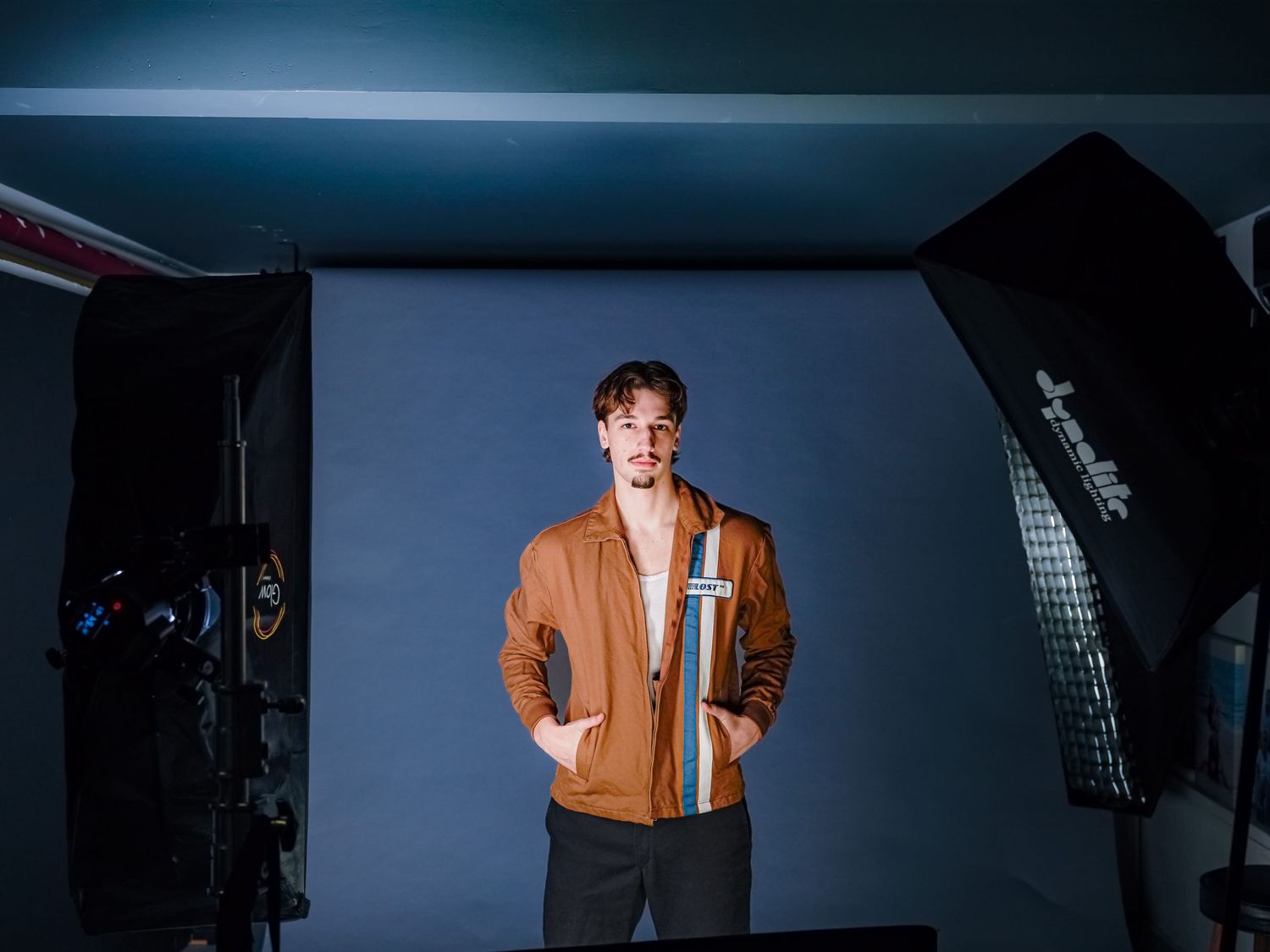 Studio photography setup with dramatic lighting and a figure in an orange jacket against a dark background.