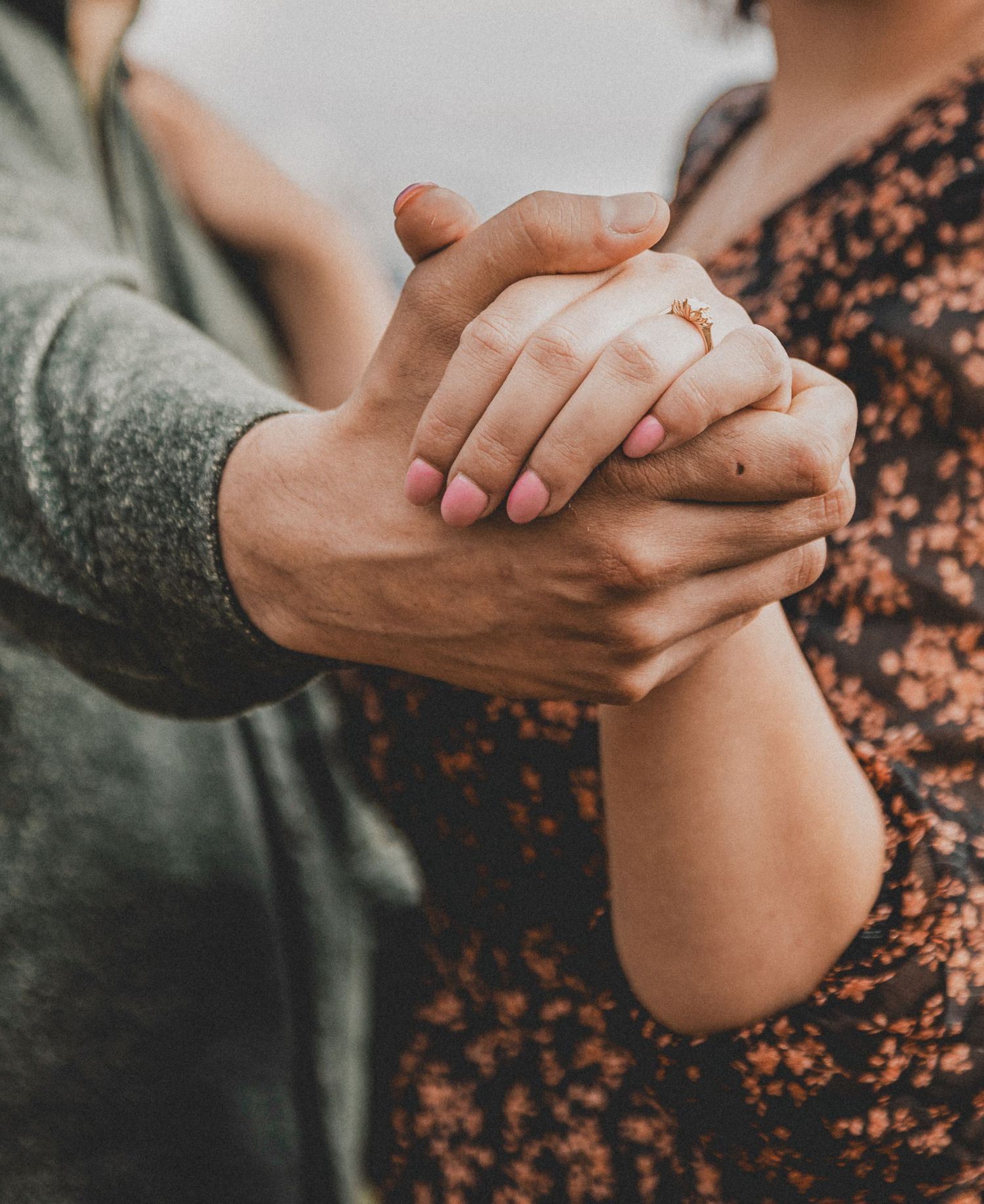 Close-up of hands holding each other with an engagement ring visible against casual clothing.