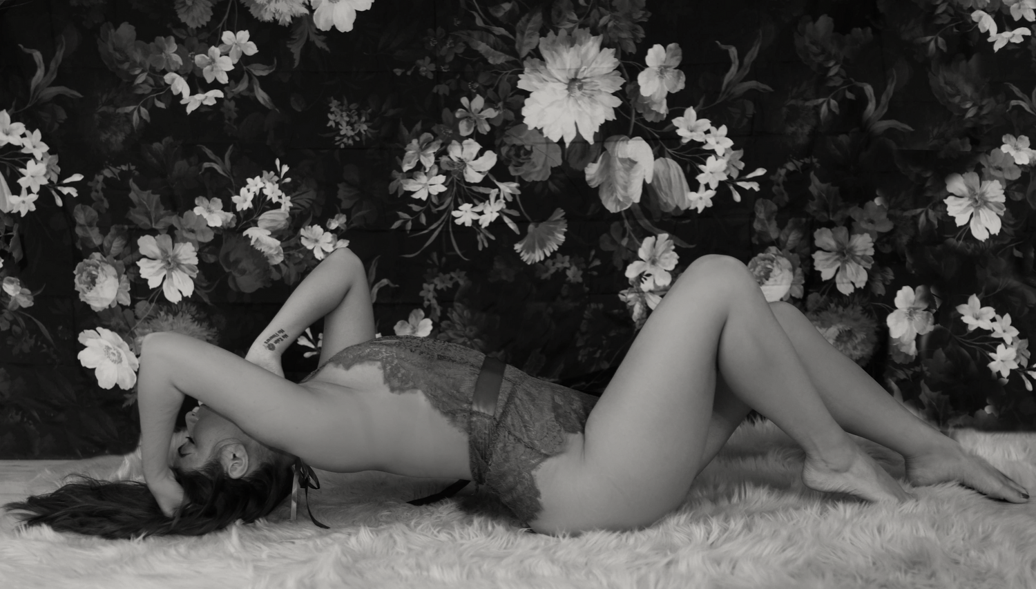 Vintage-style black and white boudoir portrait against floral backdrop.