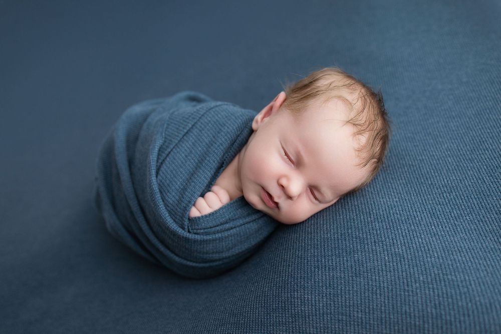 Sleeping baby wearing grey sweater lying on dark blue textured background.