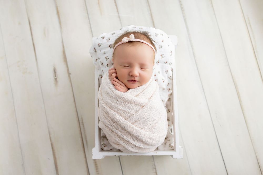 Newborn baby wrapped in white blanket lying on wooden floor in multiple artistic poses.