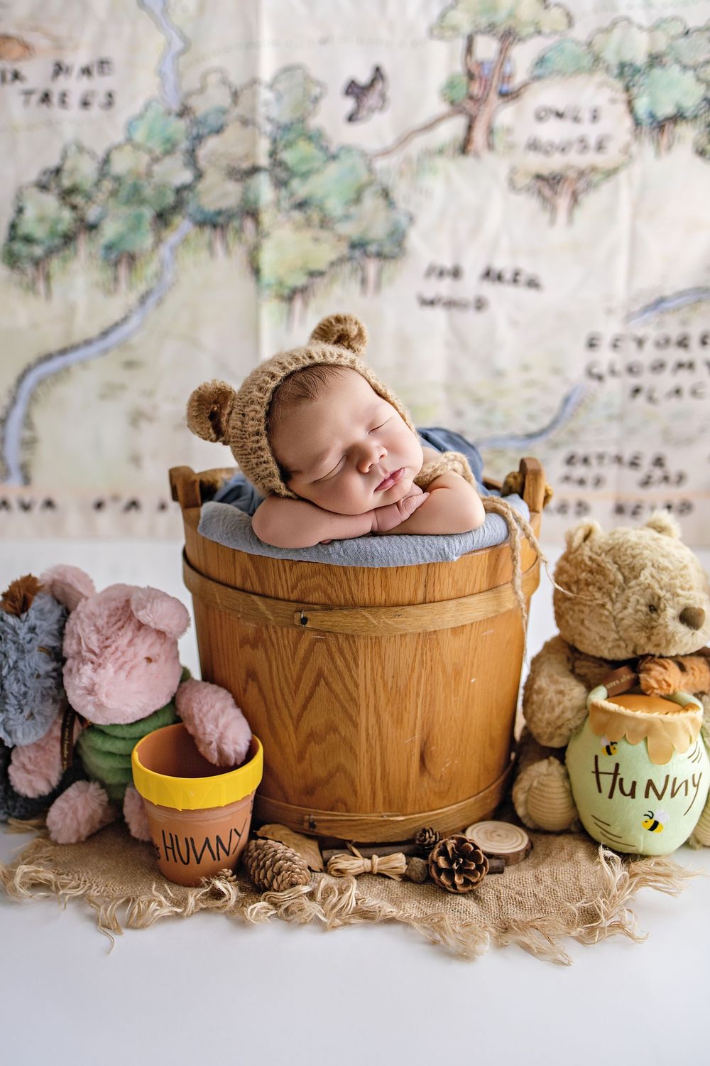 A sleeping newborn nestled in wooden barrels surrounded by plush teddy bears and soft textiles in a rustic setting.