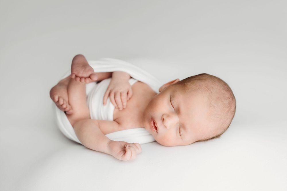A peaceful sleeping newborn baby wearing a white diaper lies curled up on a white background.