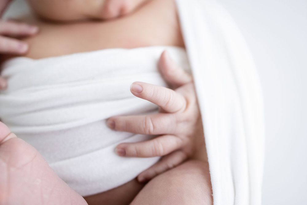 Close up of hands gently holding white fabric against skin in soft natural lighting.