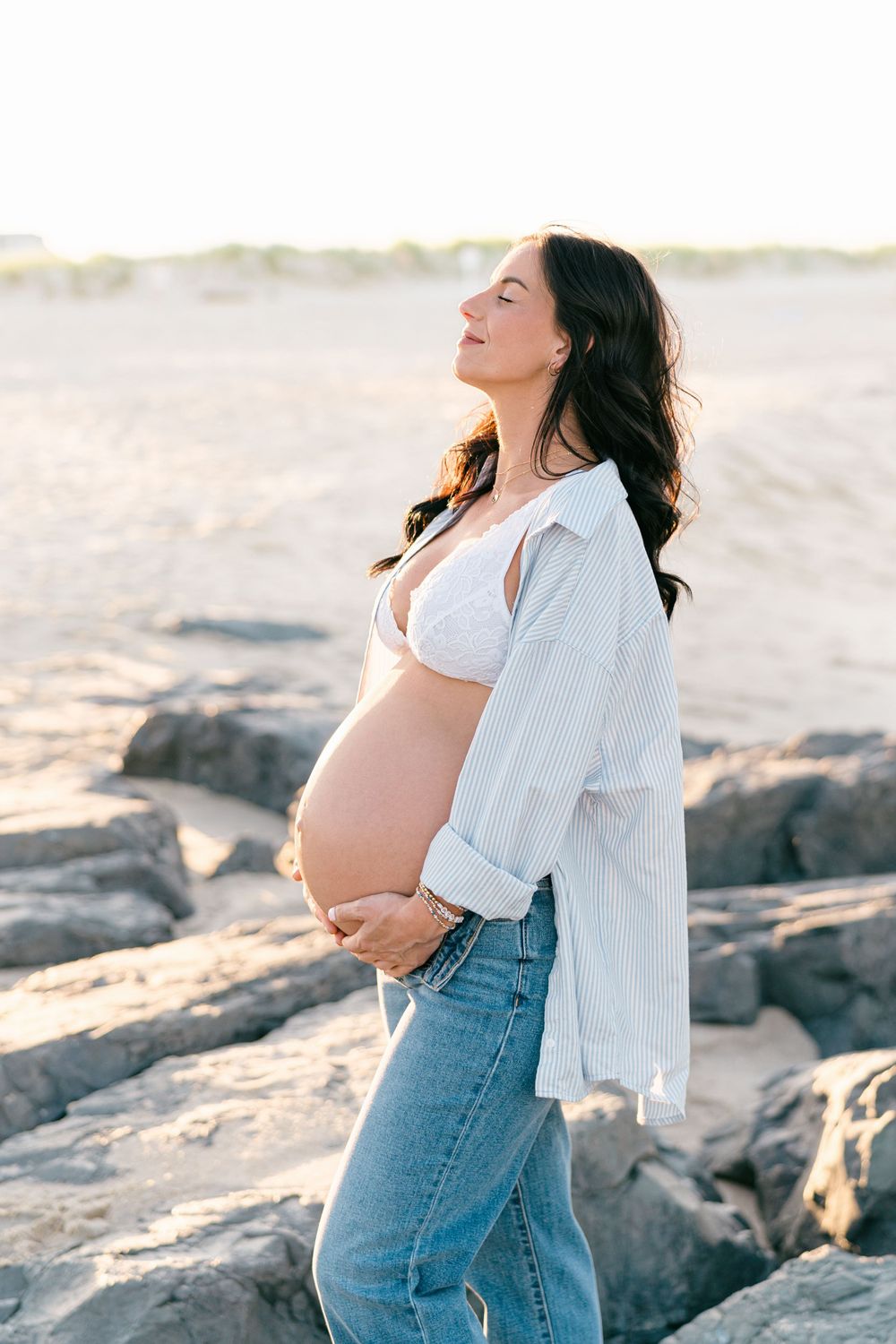 Pregnant woman standing on the beach breathing in the fresh ocean air at the beach in NJ.