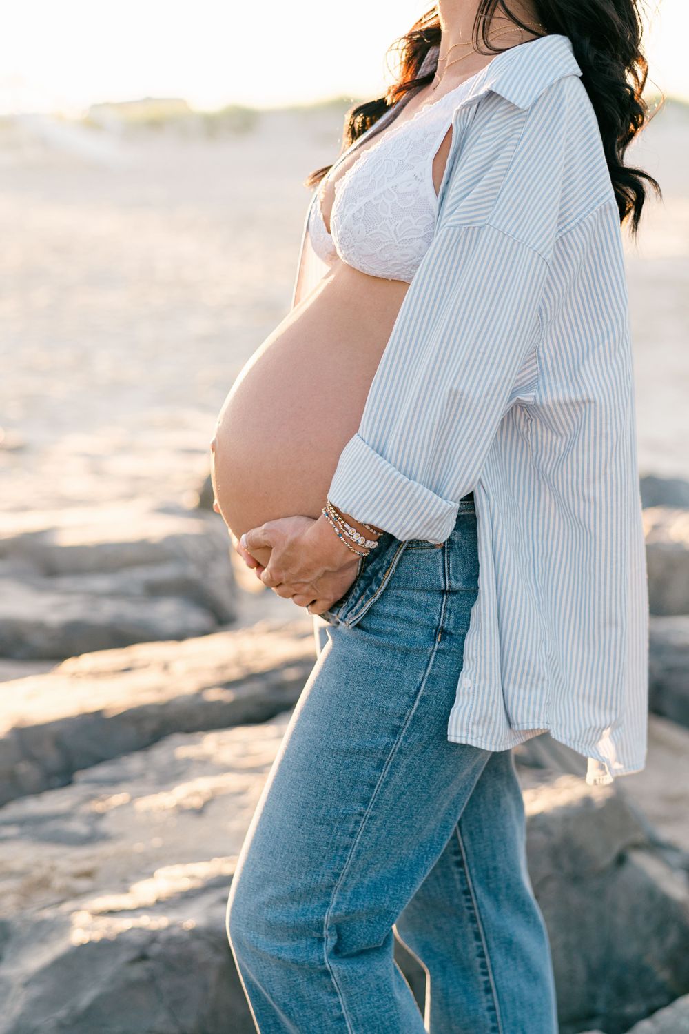 Close up of pregnant woman standing on the beach, hands resting on her belly.